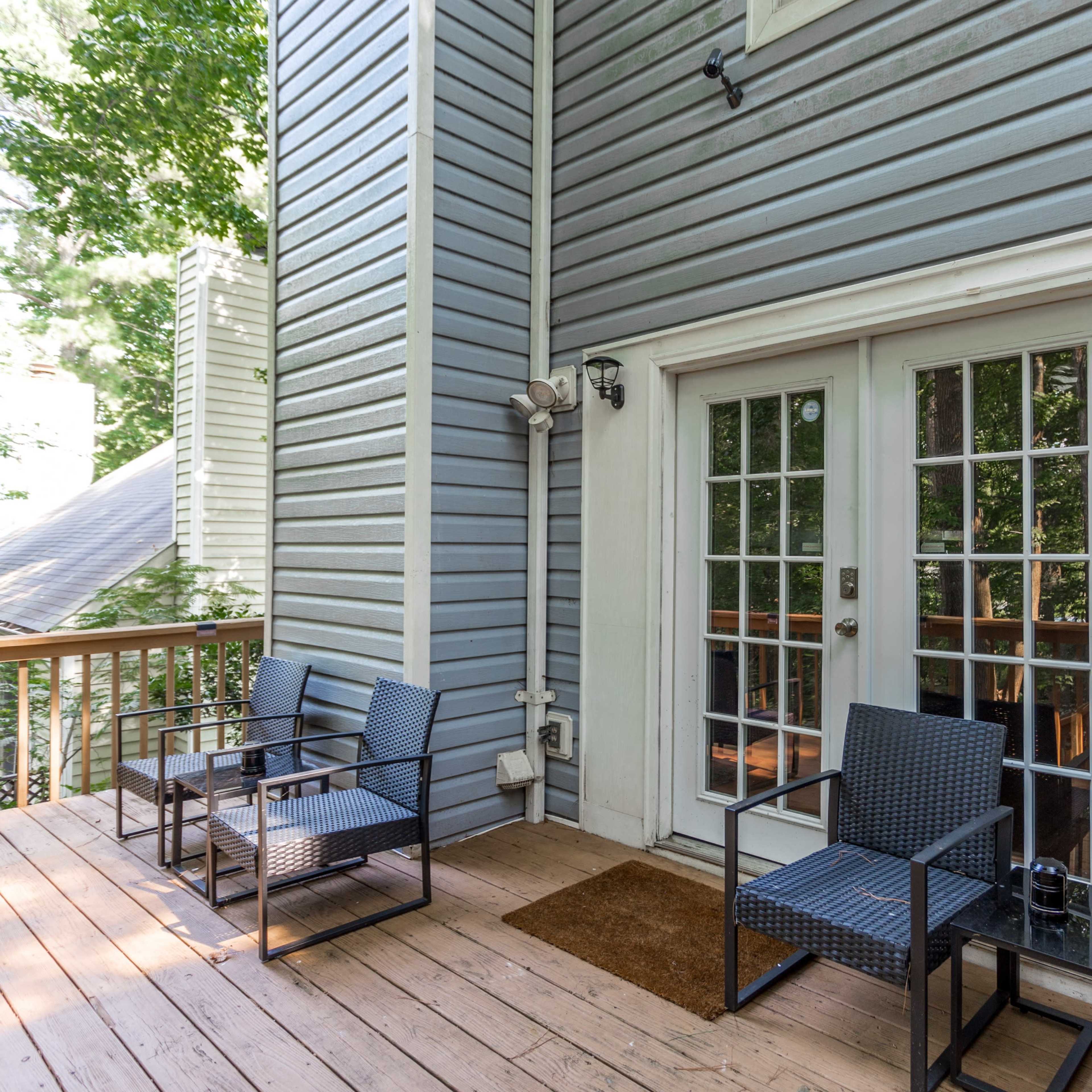 A patio with four black metal chairs and a doormat in front of a set of double glass doors leading to the interior of a house.