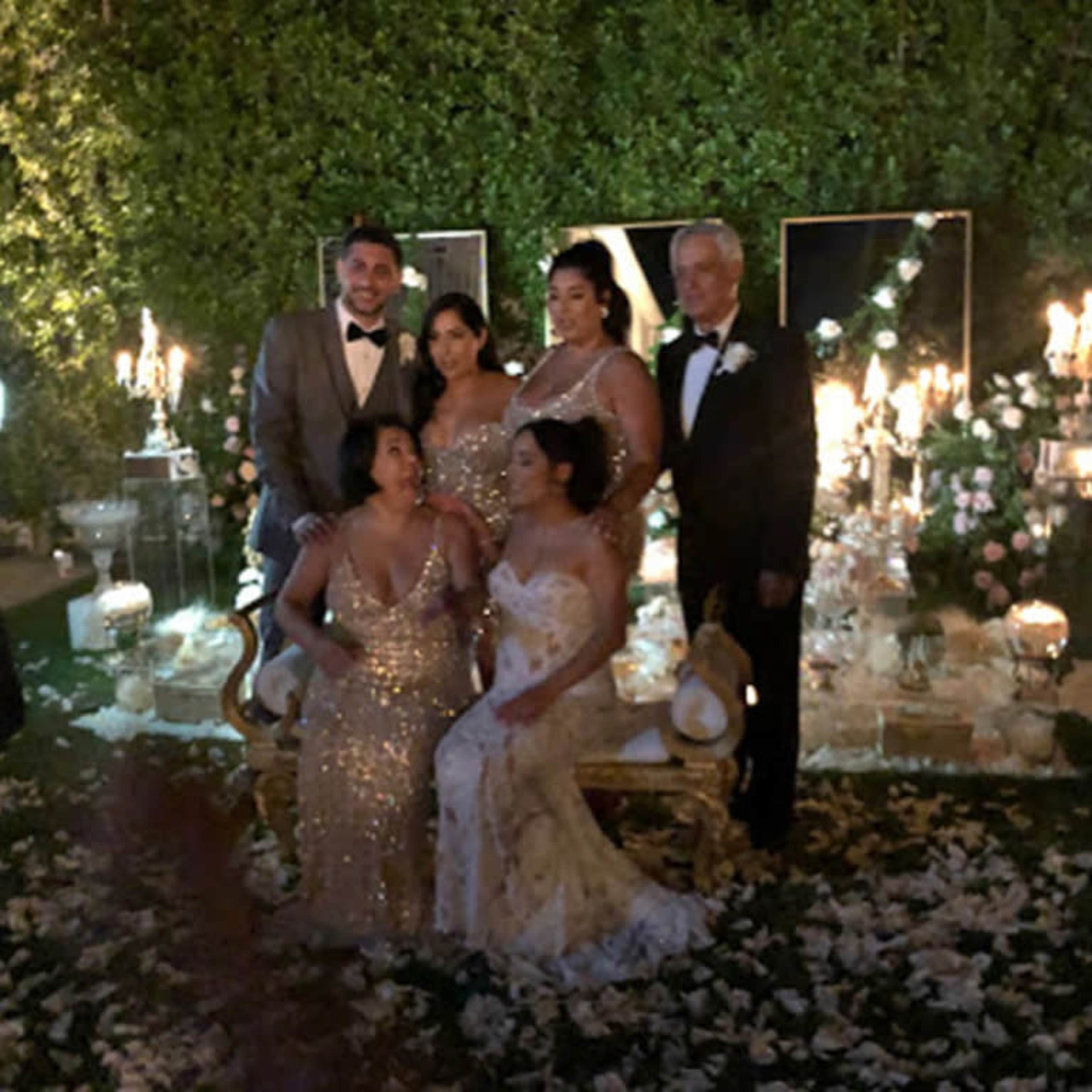 A group of six people poses for a photo in front of elegant decorations, including candles and floral arrangements, at an outdoor event.