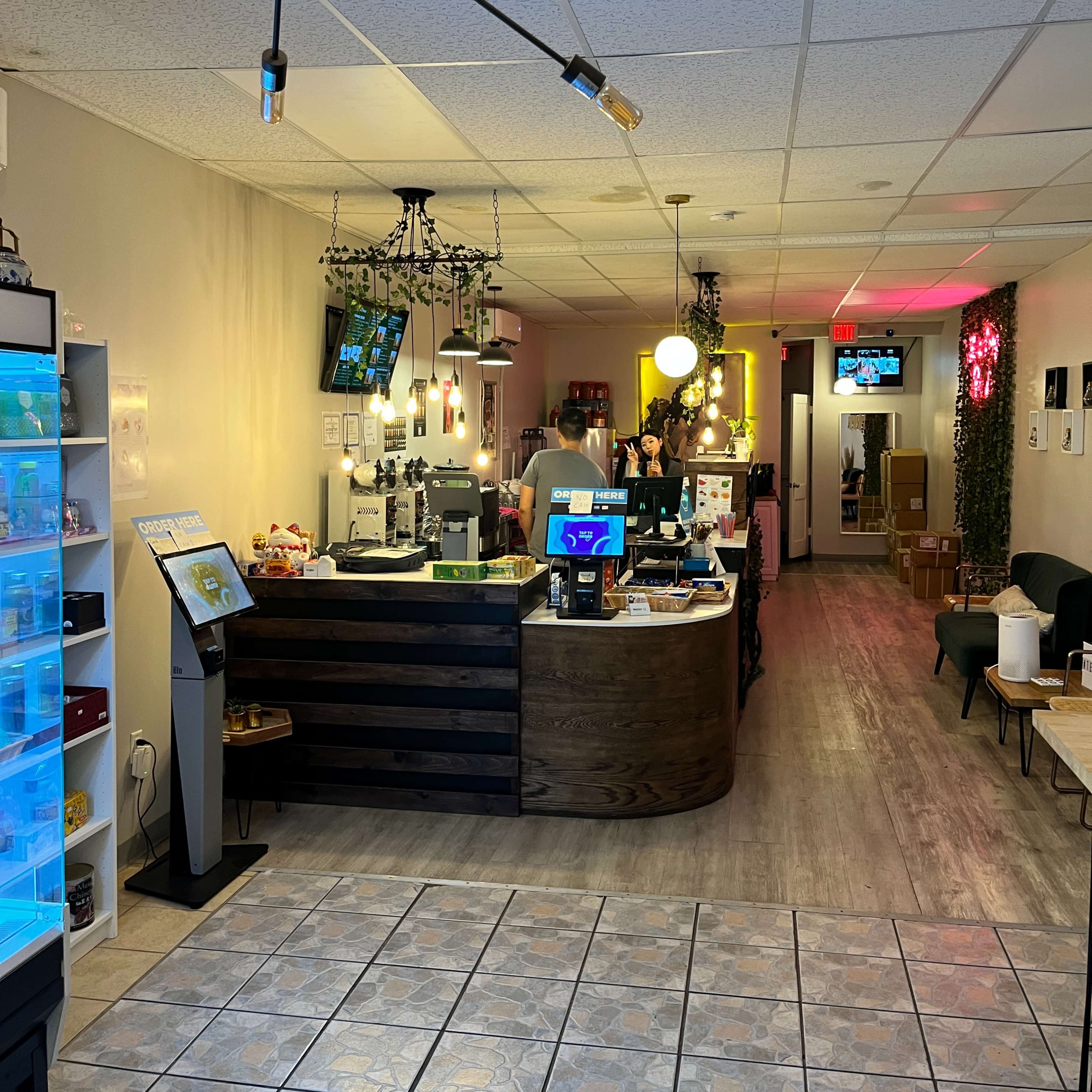 The interior of a modern café, featuring a service counter with a cash register and a variety of displays, while tables and seating are arranged in a spacious layout.