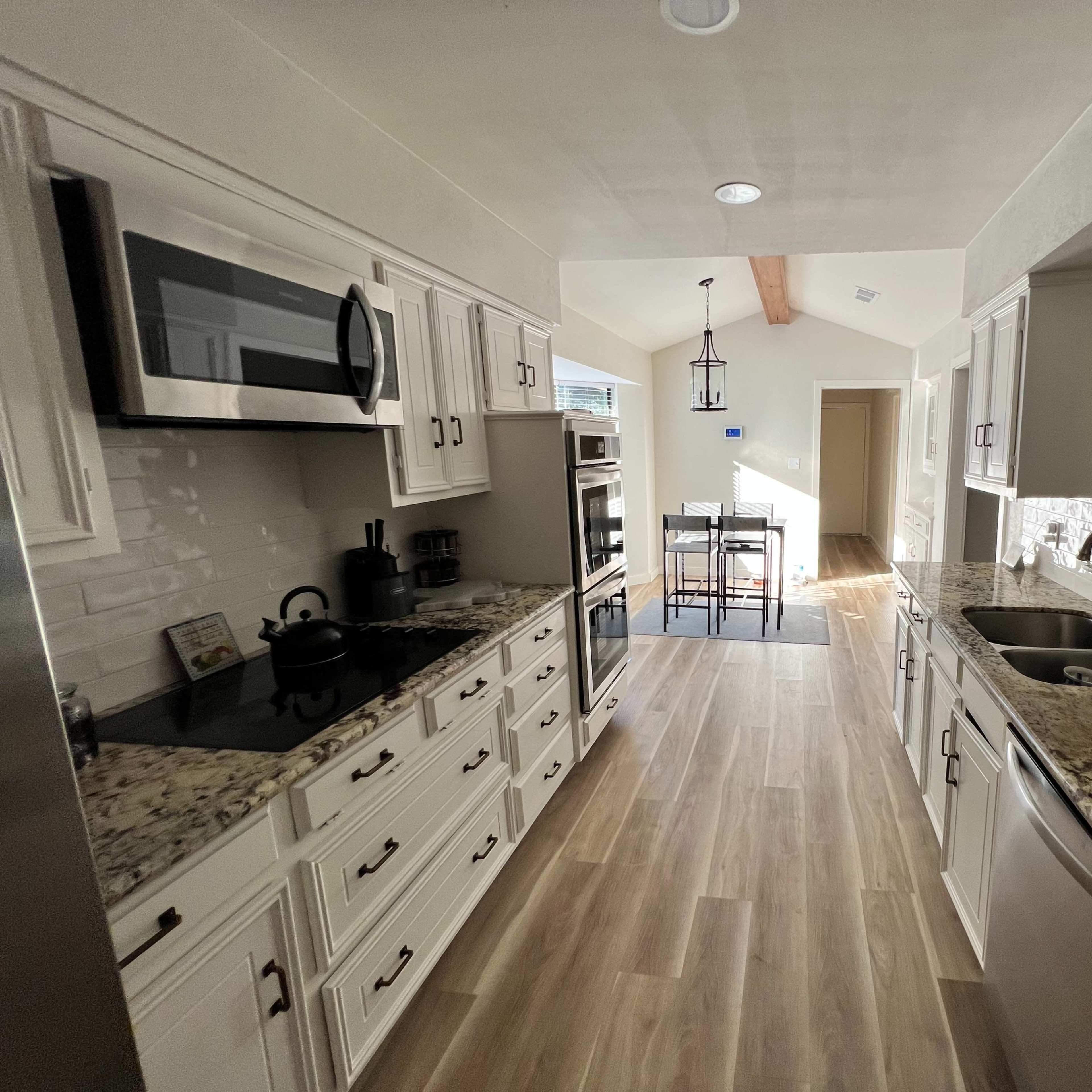 A modern kitchen with granite countertops, stainless steel appliances, and a tile floor, featuring an open layout that leads to a dining area.