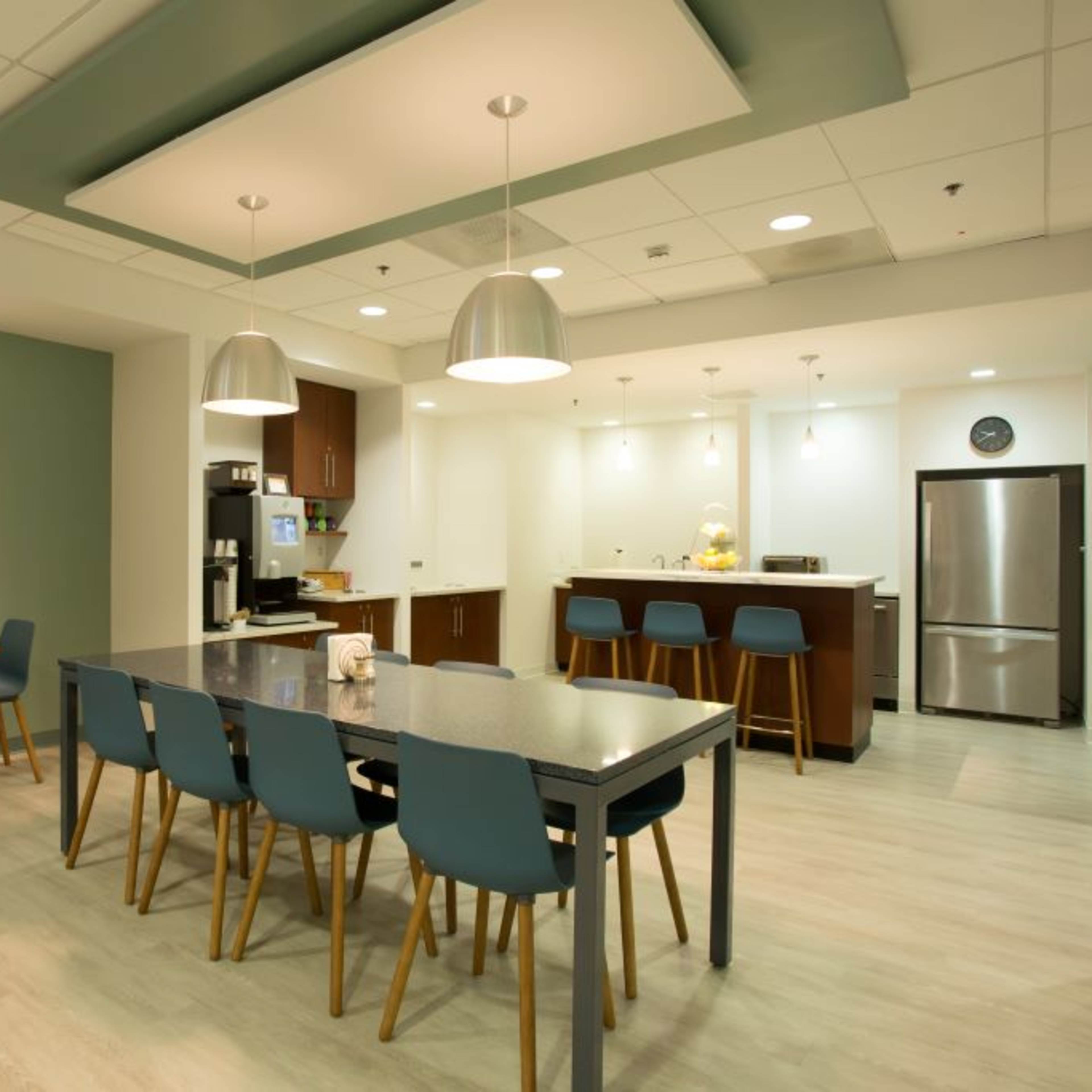 A modern kitchen and dining area with a large table, blue chairs, and a kitchenette featuring stainless steel appliances.