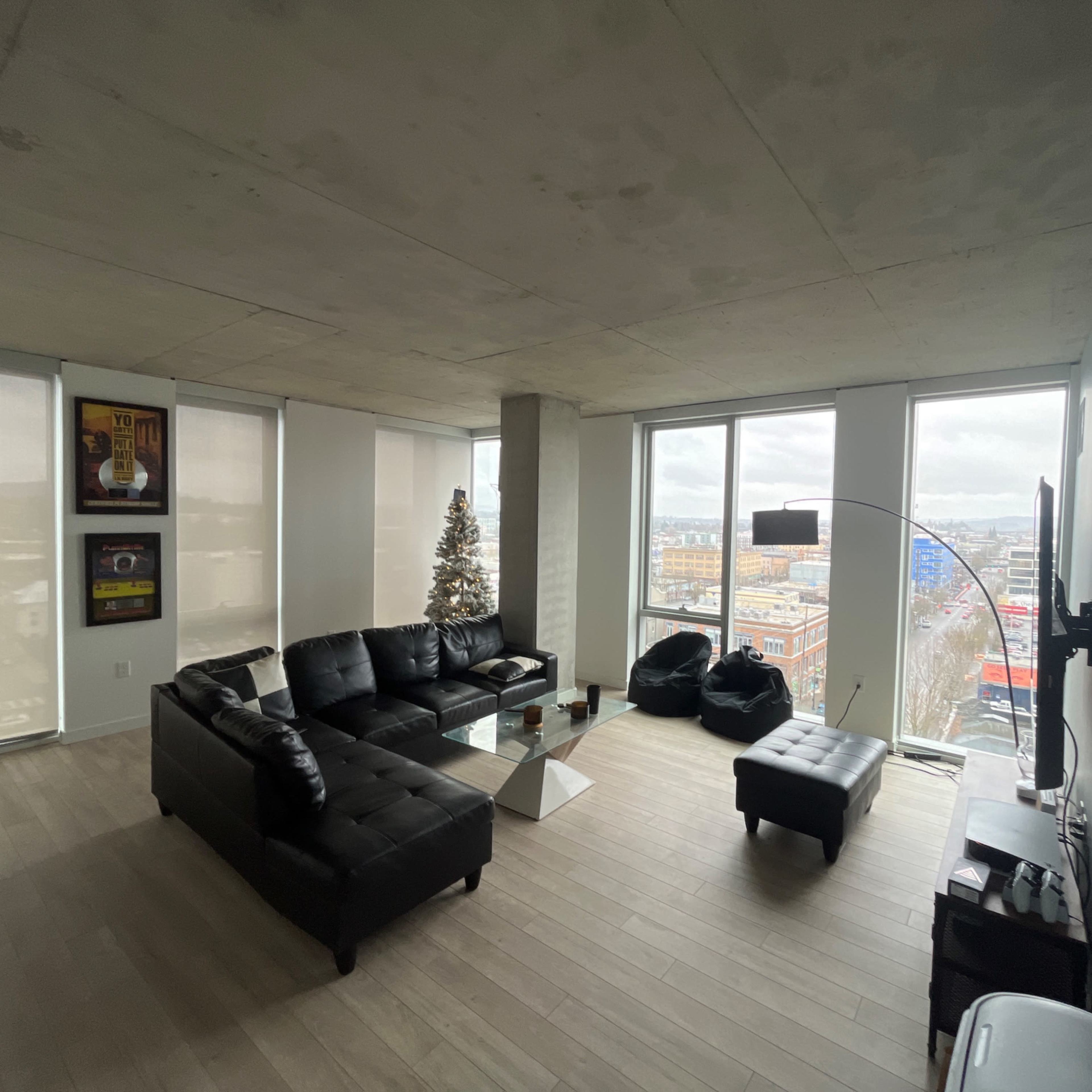 A modern living room with a black sectional sofa, a glass coffee table, and large windows providing a view of the city skyline.