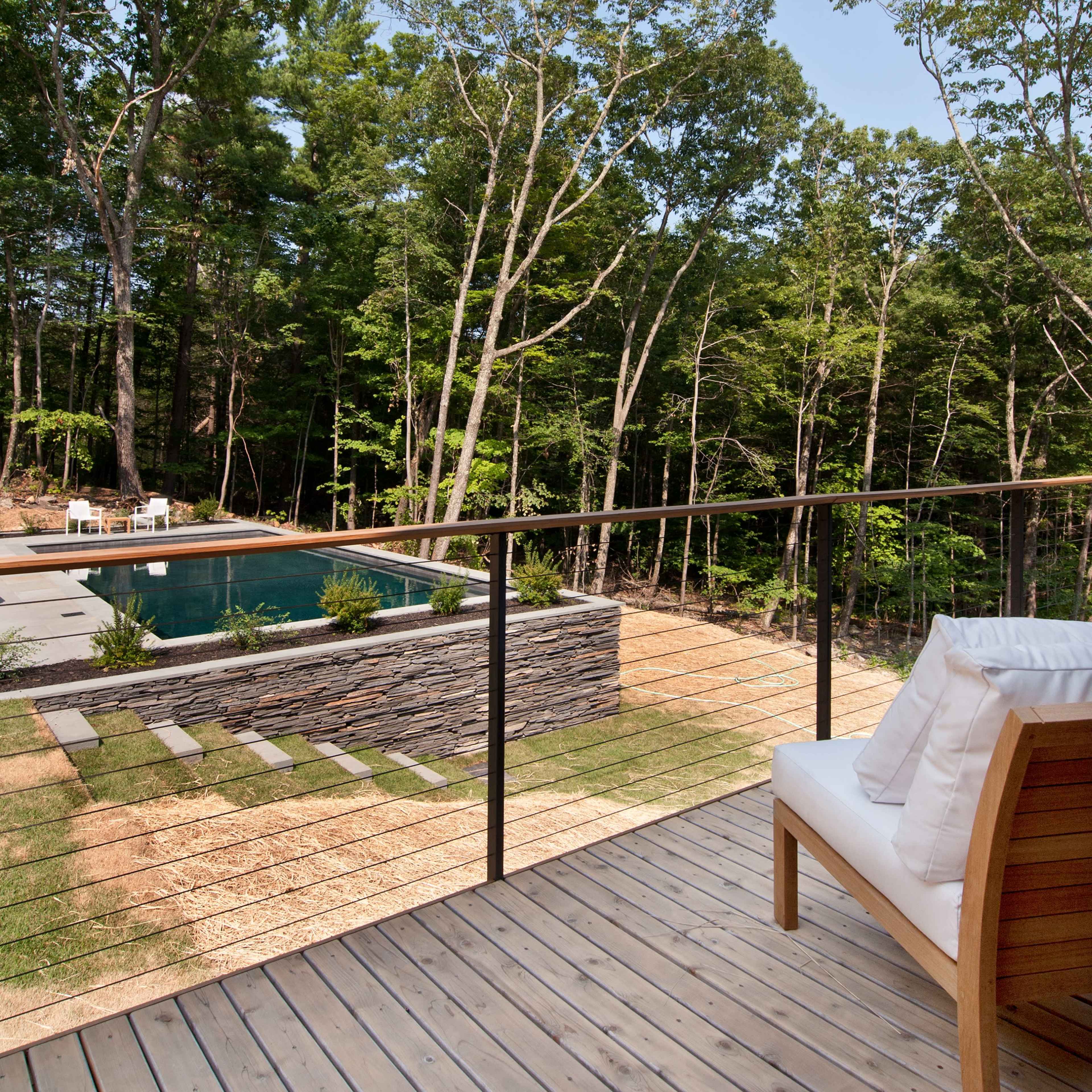 A wooden deck overlooks a stone-walled swimming pool surrounded by trees and landscaped grass.