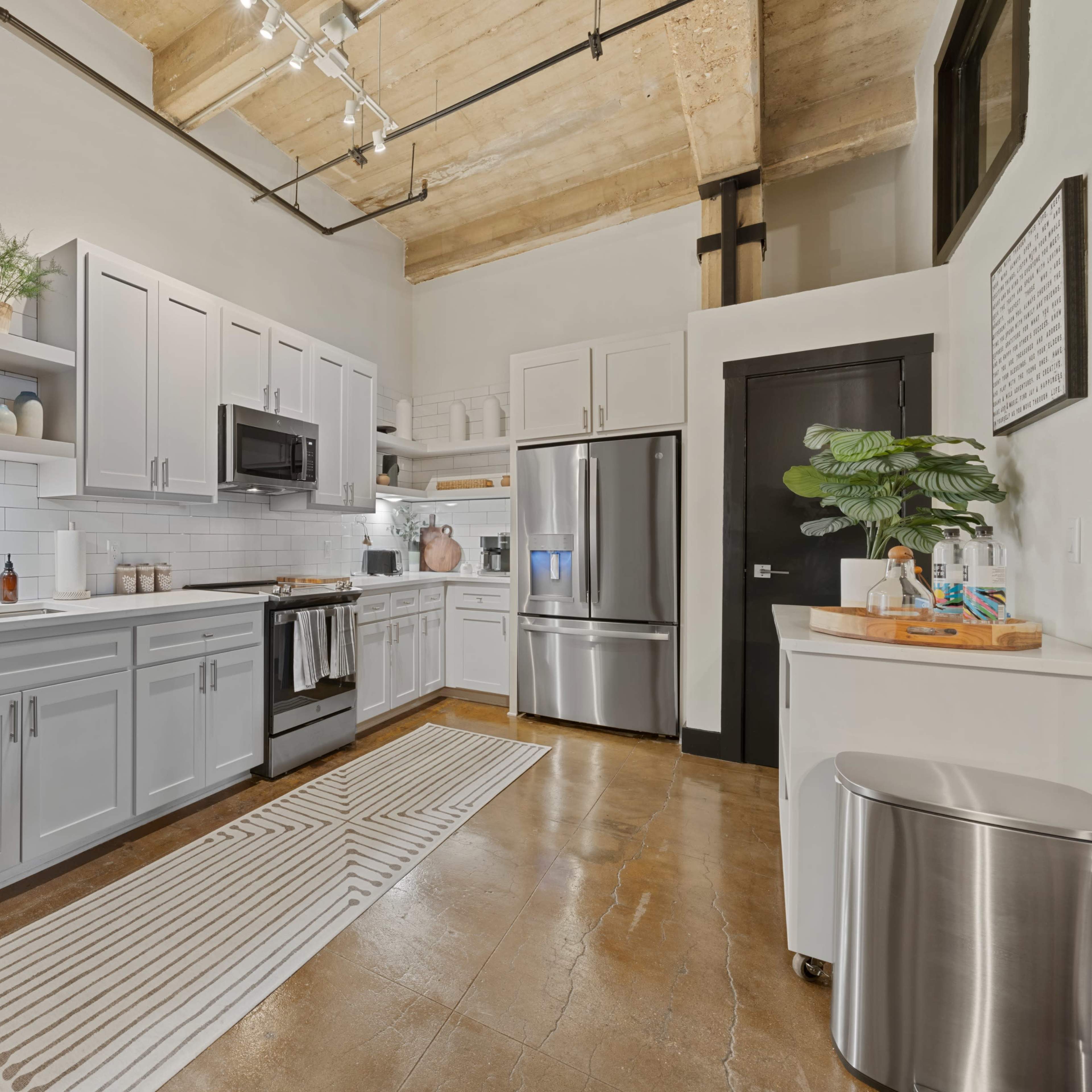 A modern kitchen features white cabinetry, stainless steel appliances, and an island with a decorative bowl, set against a backdrop of exposed wood beams.