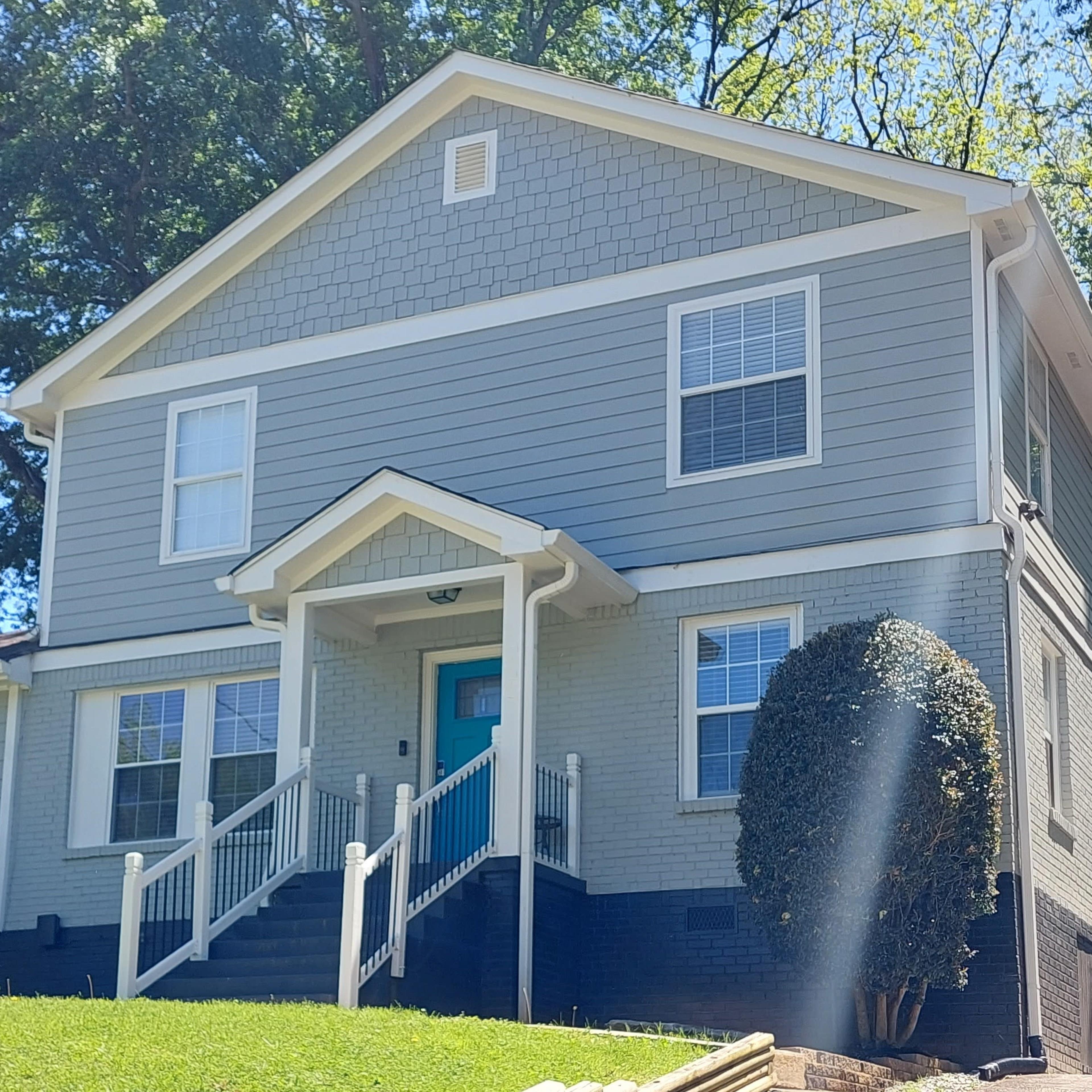 A two-story gray house with white trim, a teal front door, and a lawn that is well-maintained.