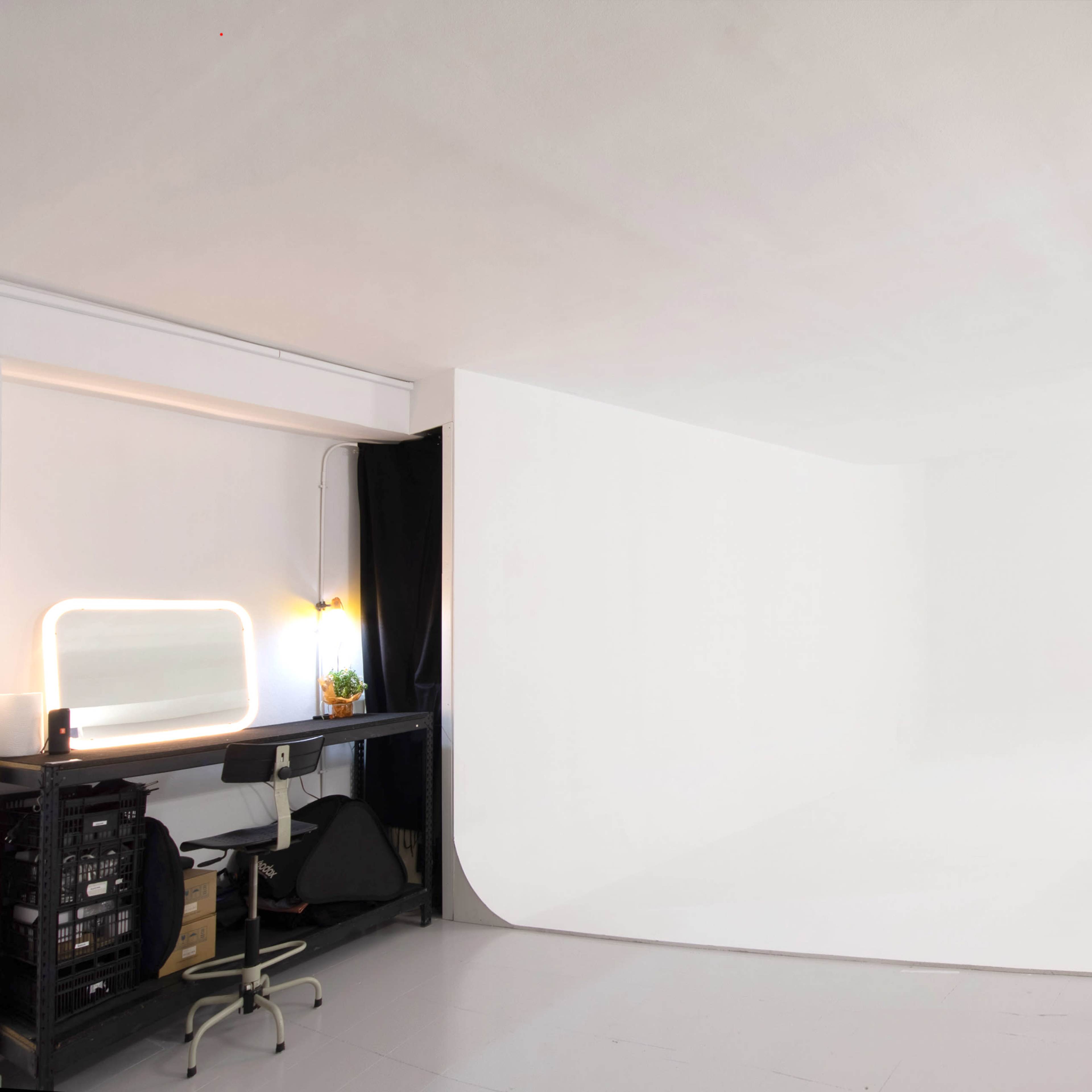A photography studio with a seamless white backdrop and various lighting equipment arranged to the side.