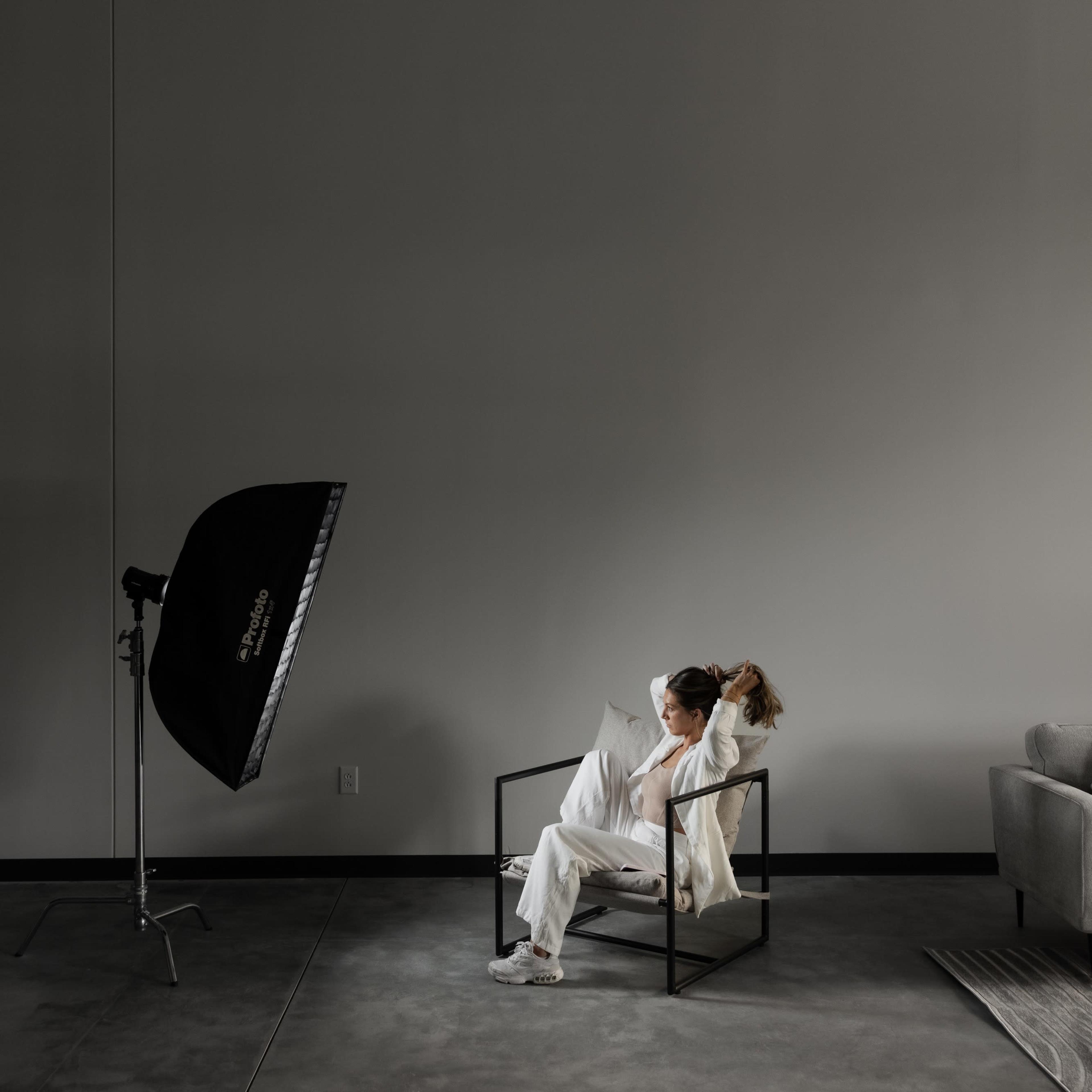 A person sits in a modern chair in a minimalistic room with a large light source positioned nearby.