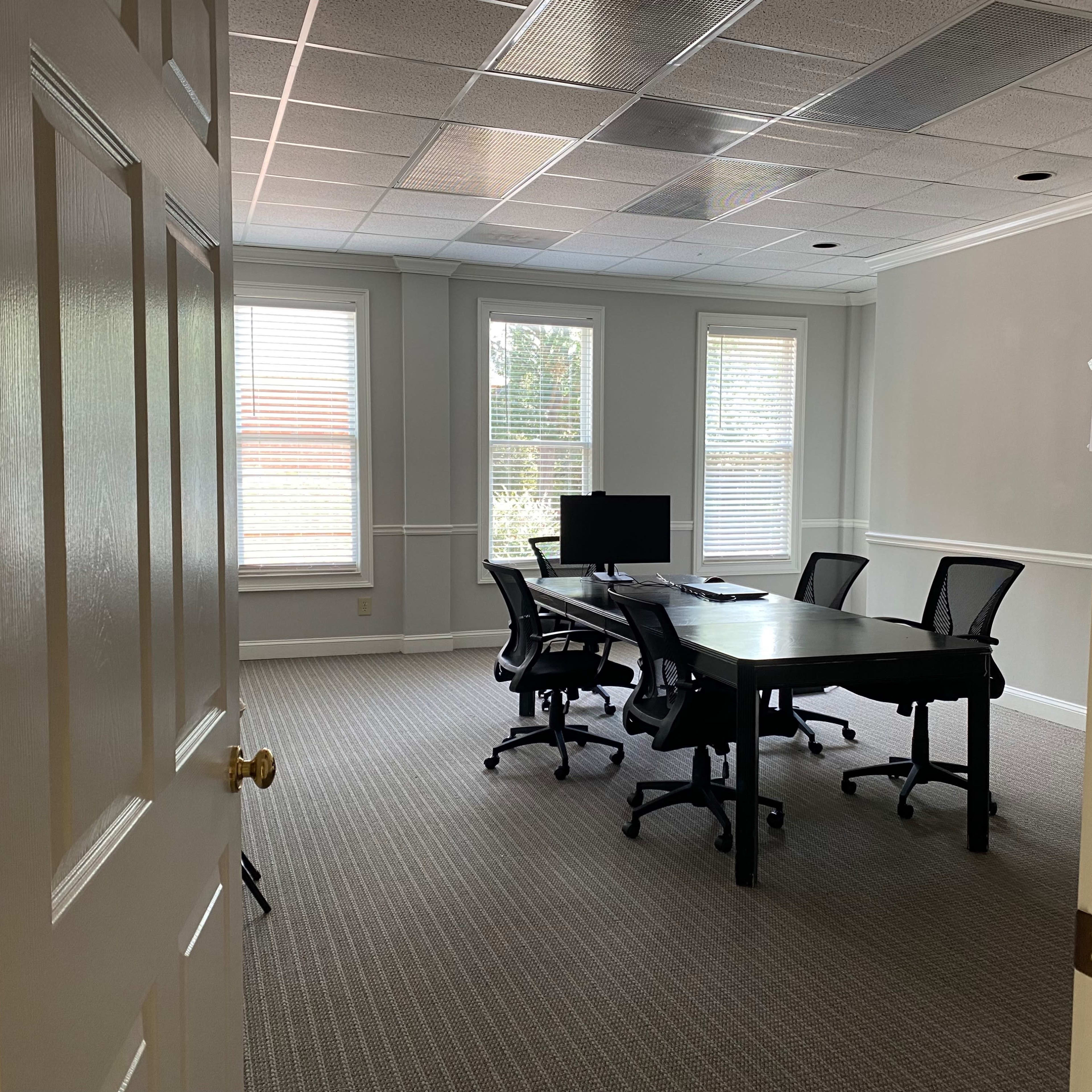 A vacant conference room with a large table, four chairs, and a computer monitor is visible through an open door.