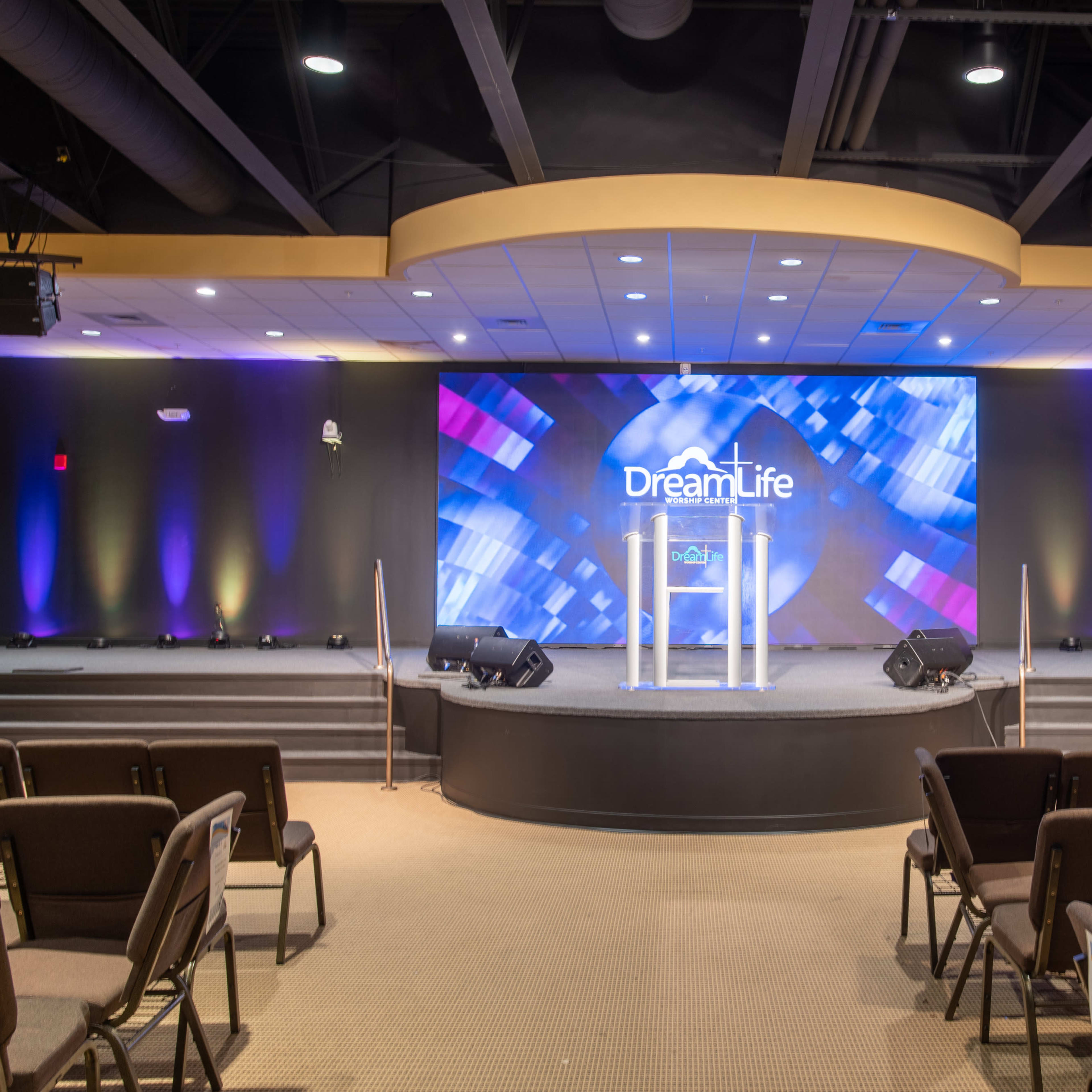 A church stage with a podium, a backdrop featuring "Dream Life," and seating arranged in front.