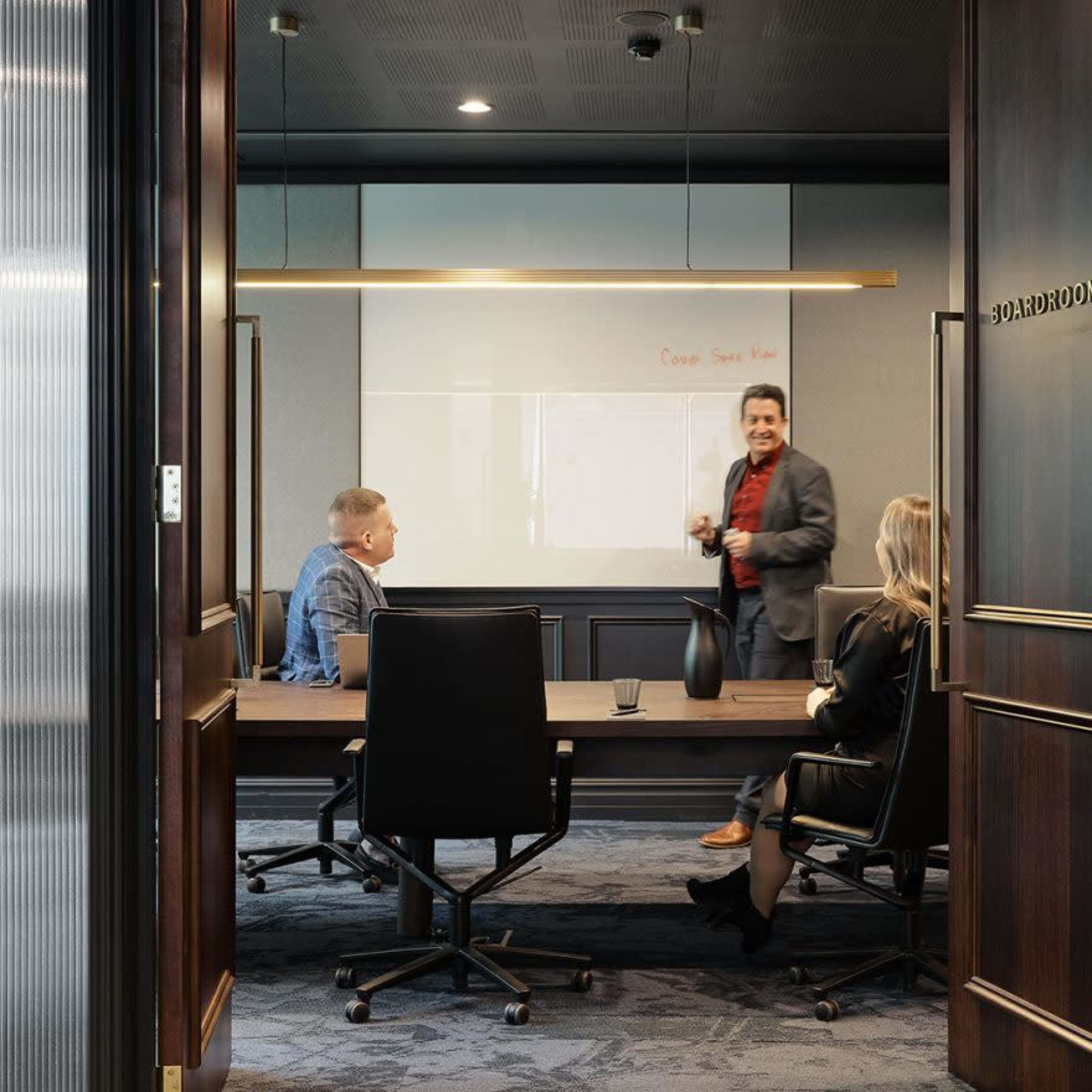 A man presents to two colleagues in a conference room with a large screen displaying information.