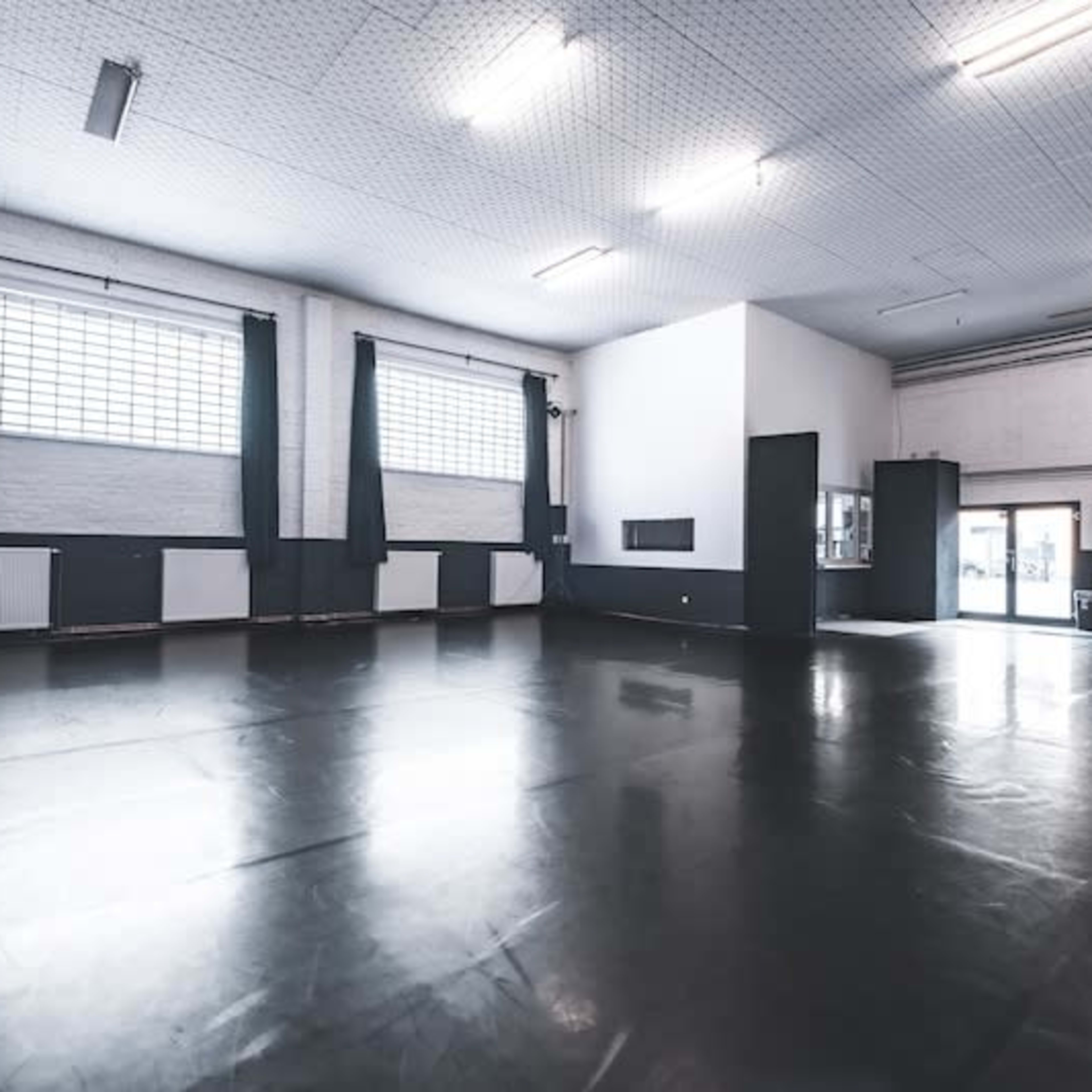 An empty dance studio with a dark floor, large windows, and white walls.