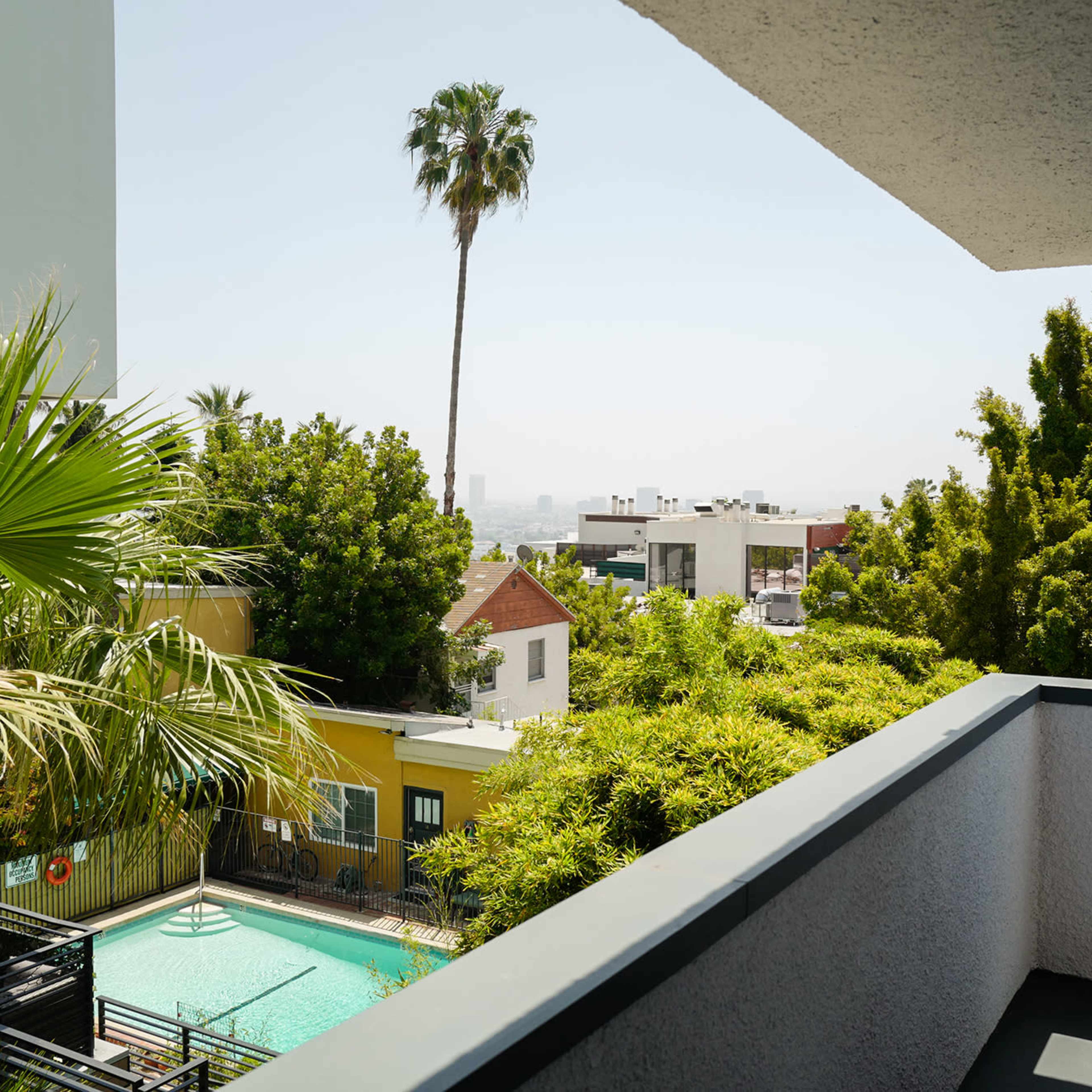 A balcony view overlooking a small pool surrounded by greenery and residential buildings in a sunny setting.