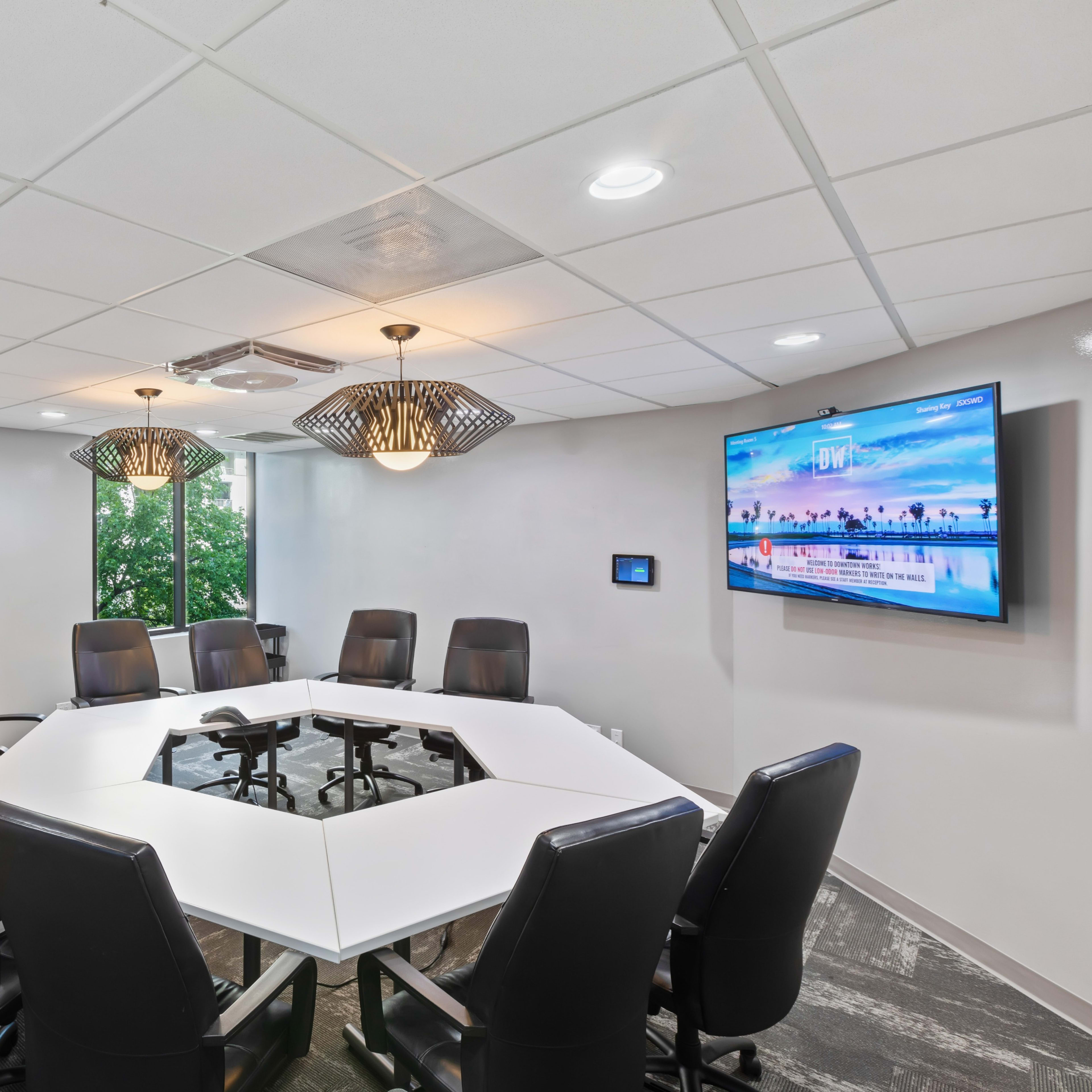 A modern conference room with a large octagonal table surrounded by black leather chairs and a wall-mounted television displaying a scenic image.
