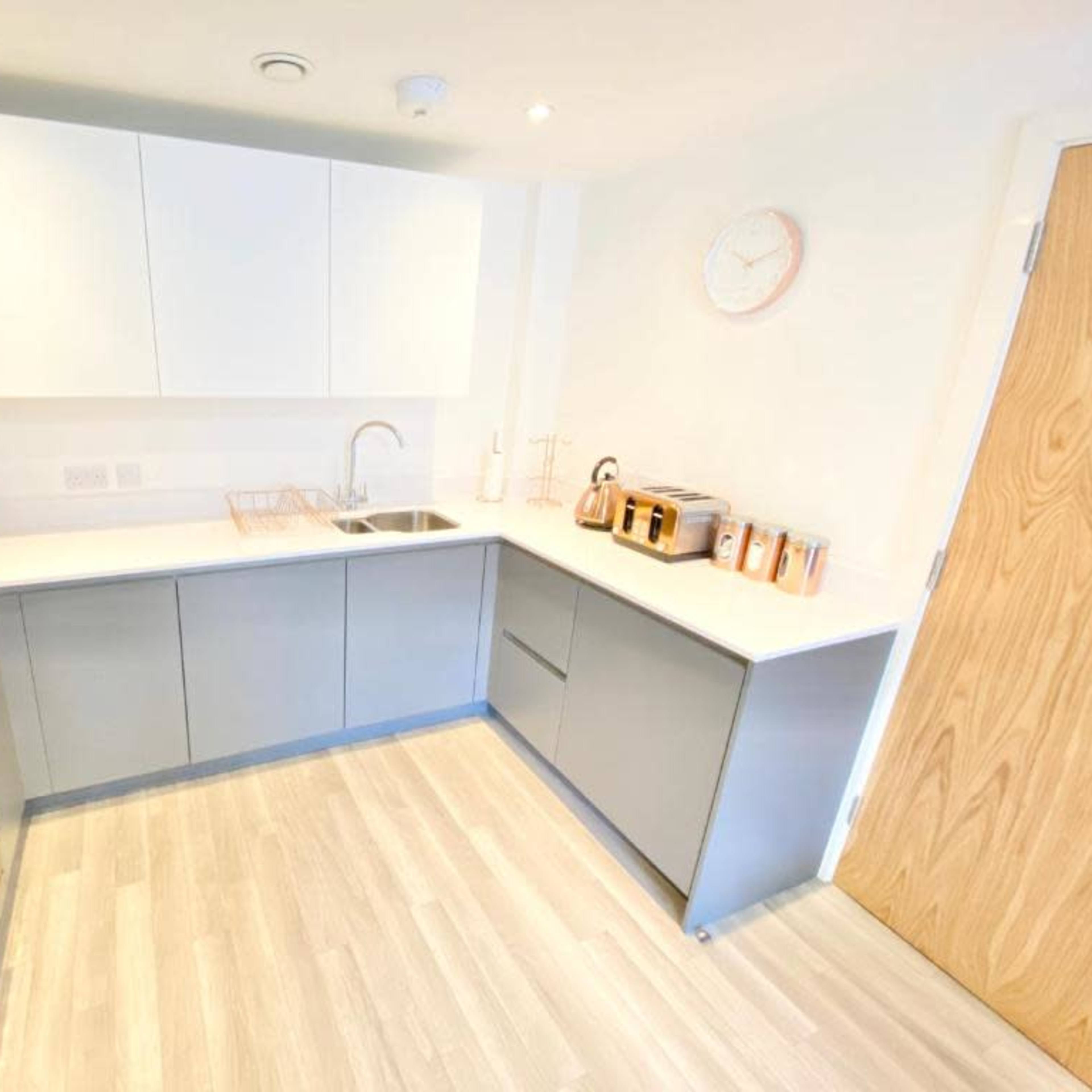 A modern kitchen with light gray and white cabinetry, a sink, a microwave, and several kitchen appliances neatly arranged on the counter.