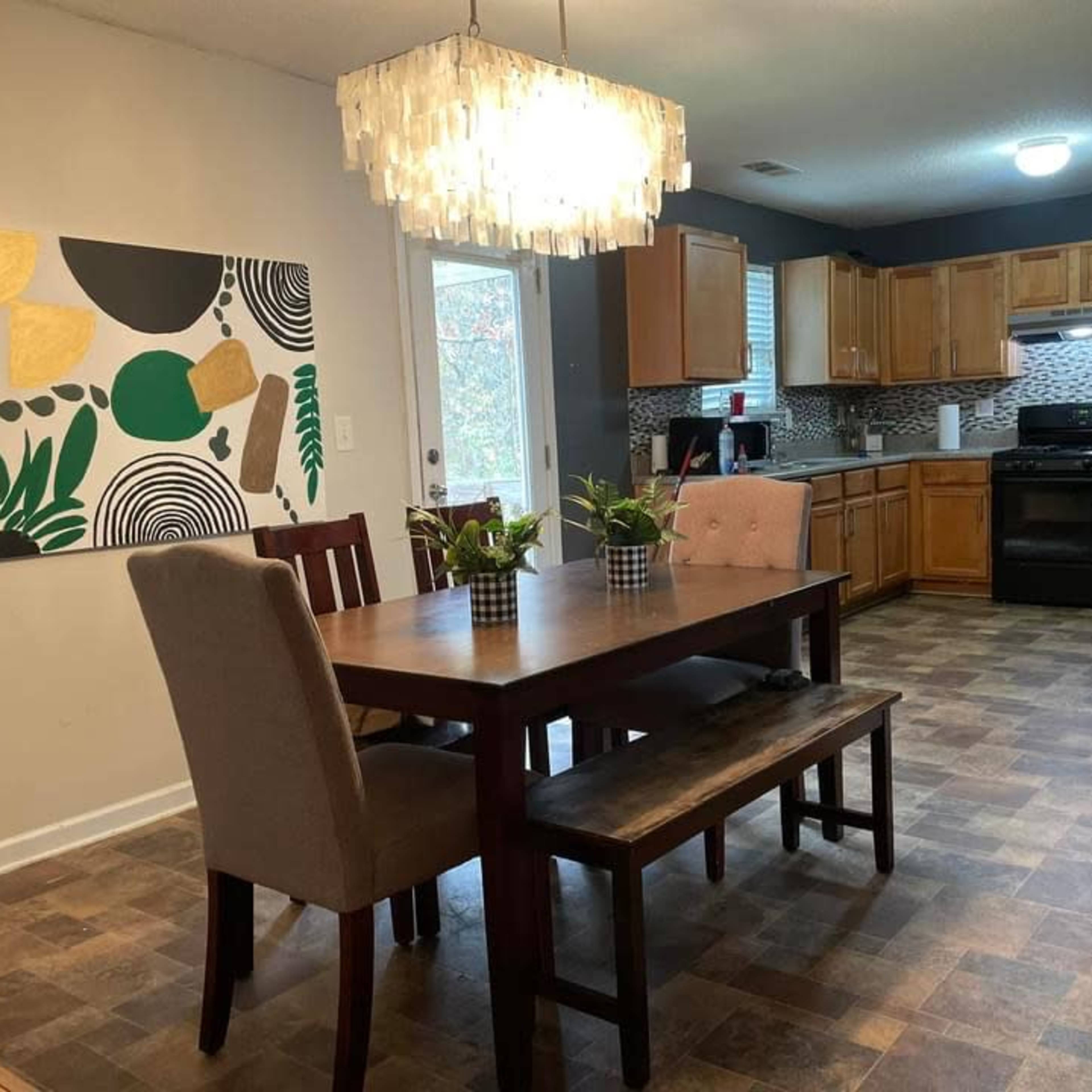 A dining area features a wooden table with seating, surrounded by a modern kitchen with cabinets and a patterned backsplash.