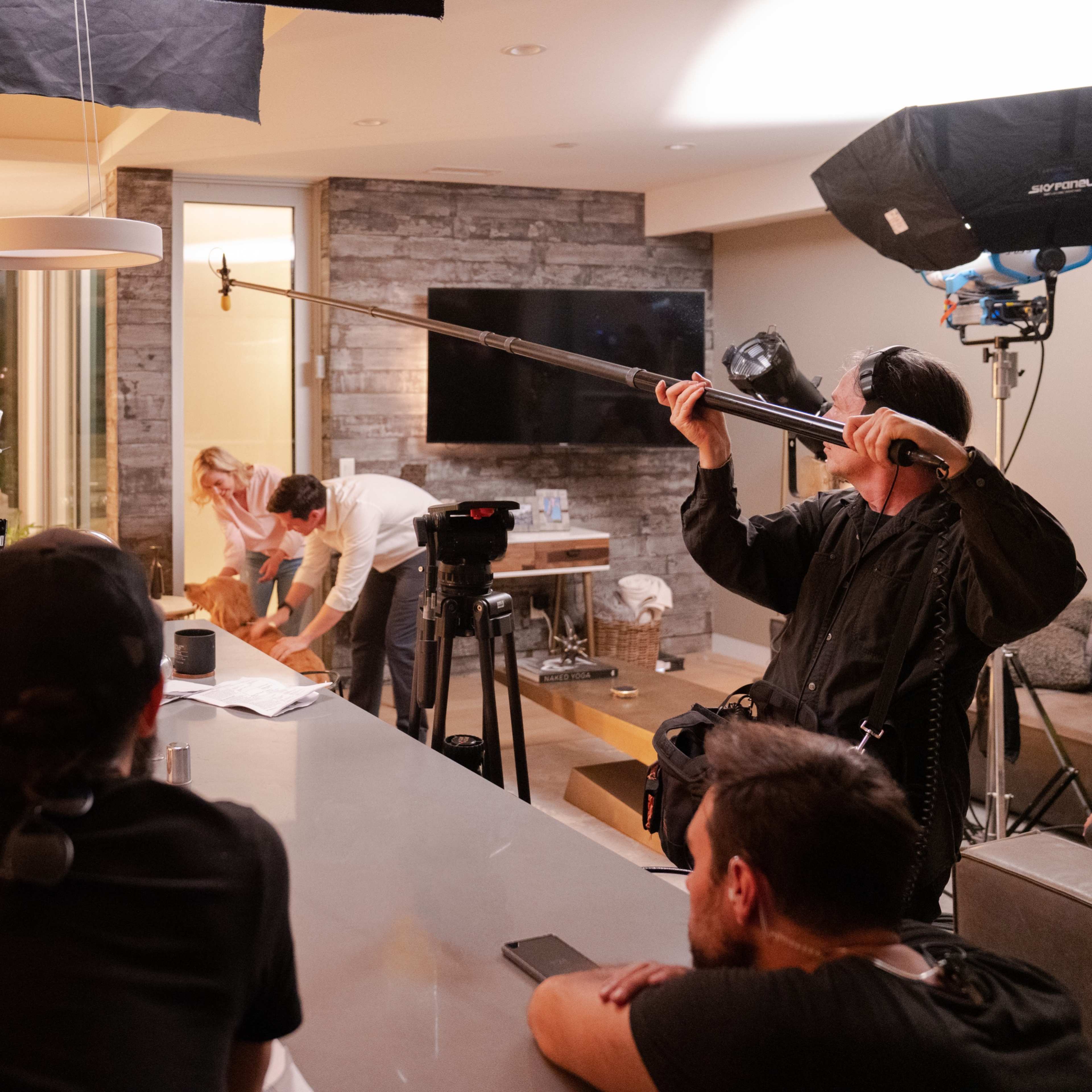 A film crew sets up for a shooting in a modern living room while a woman prepares a scene.