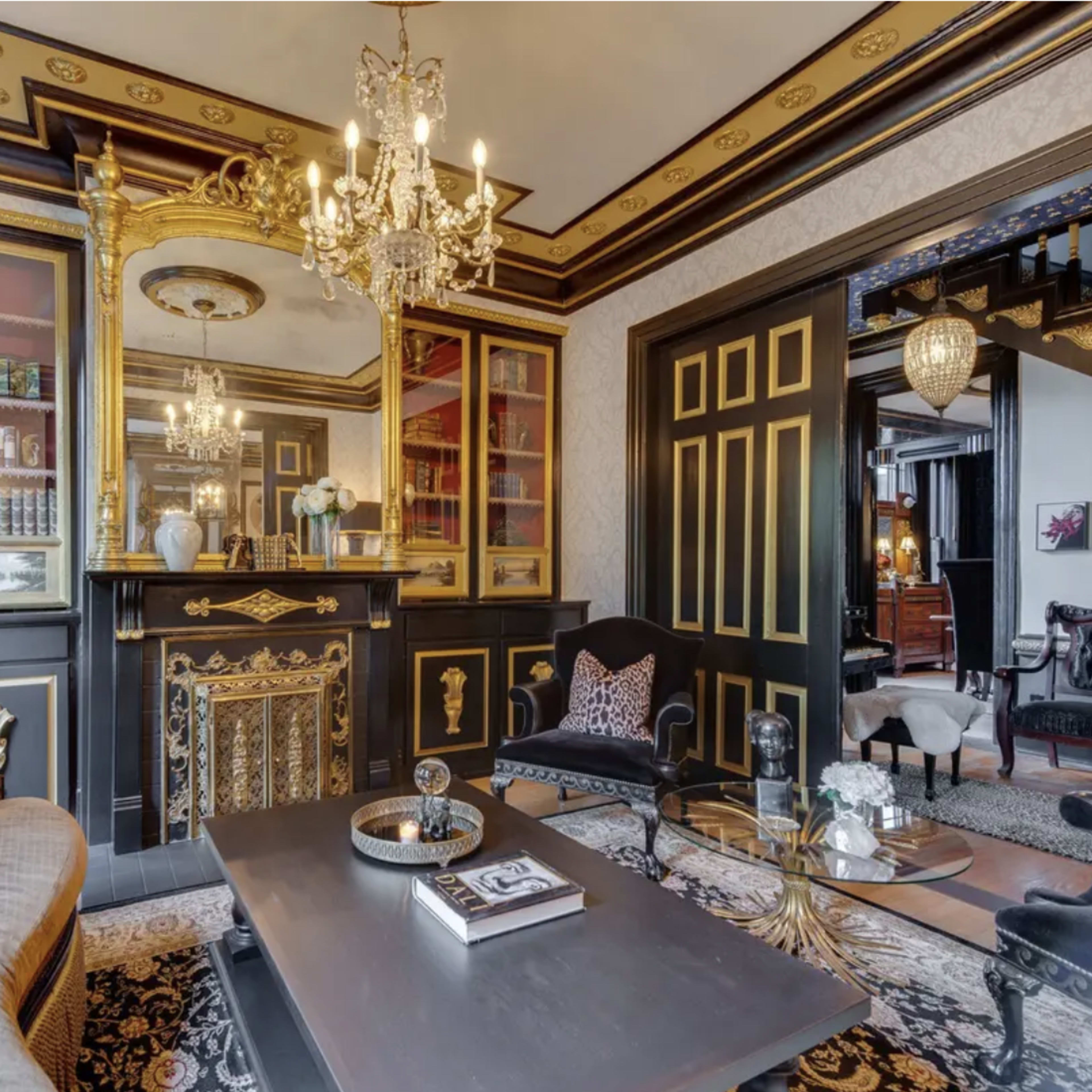 A luxurious living room featuring ornate gold accents, a decorative fireplace, and a variety of books displayed in glass-fronted cabinets.