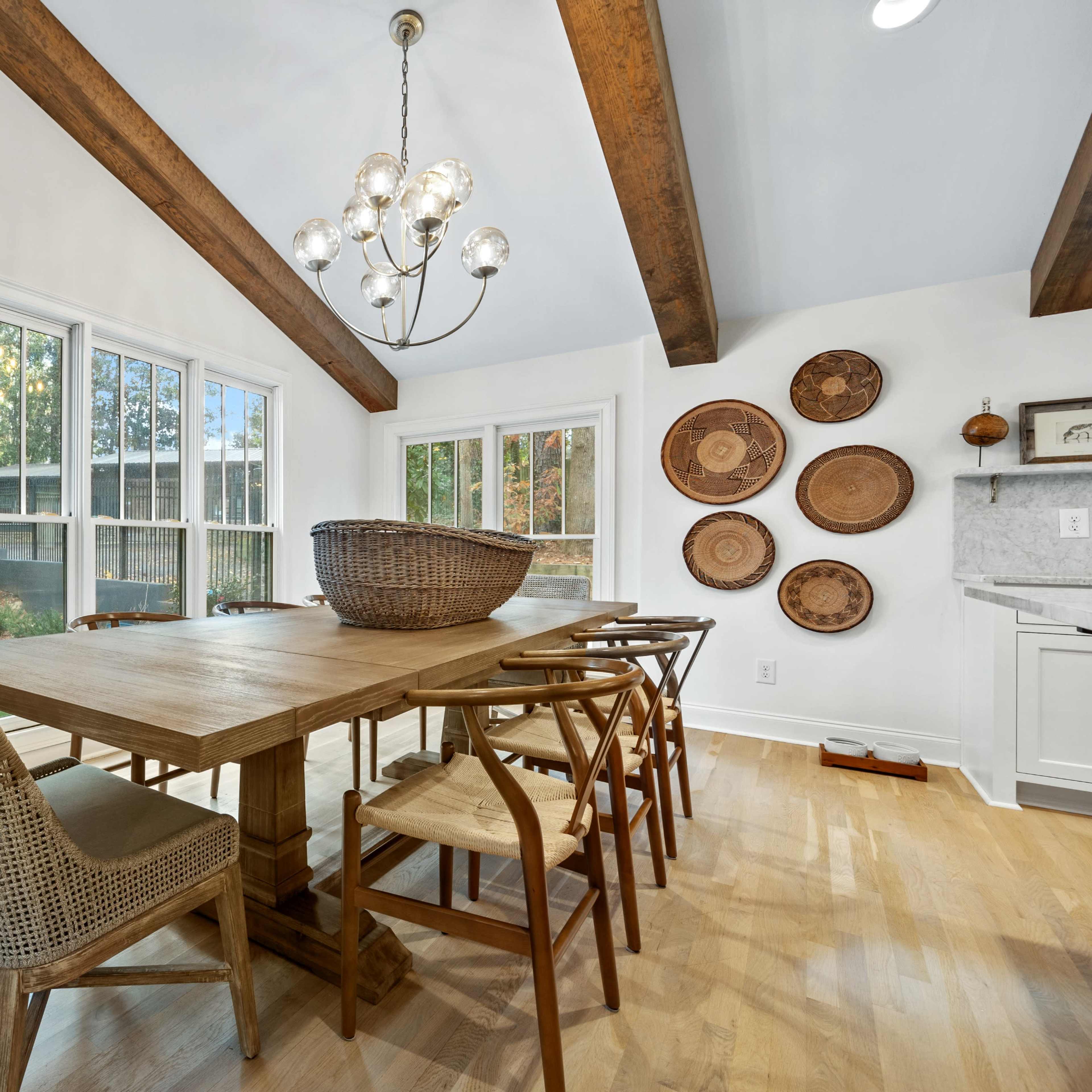 A spacious dining room featuring a wooden table surrounded by various chairs, with large windows and decorative wall elements.