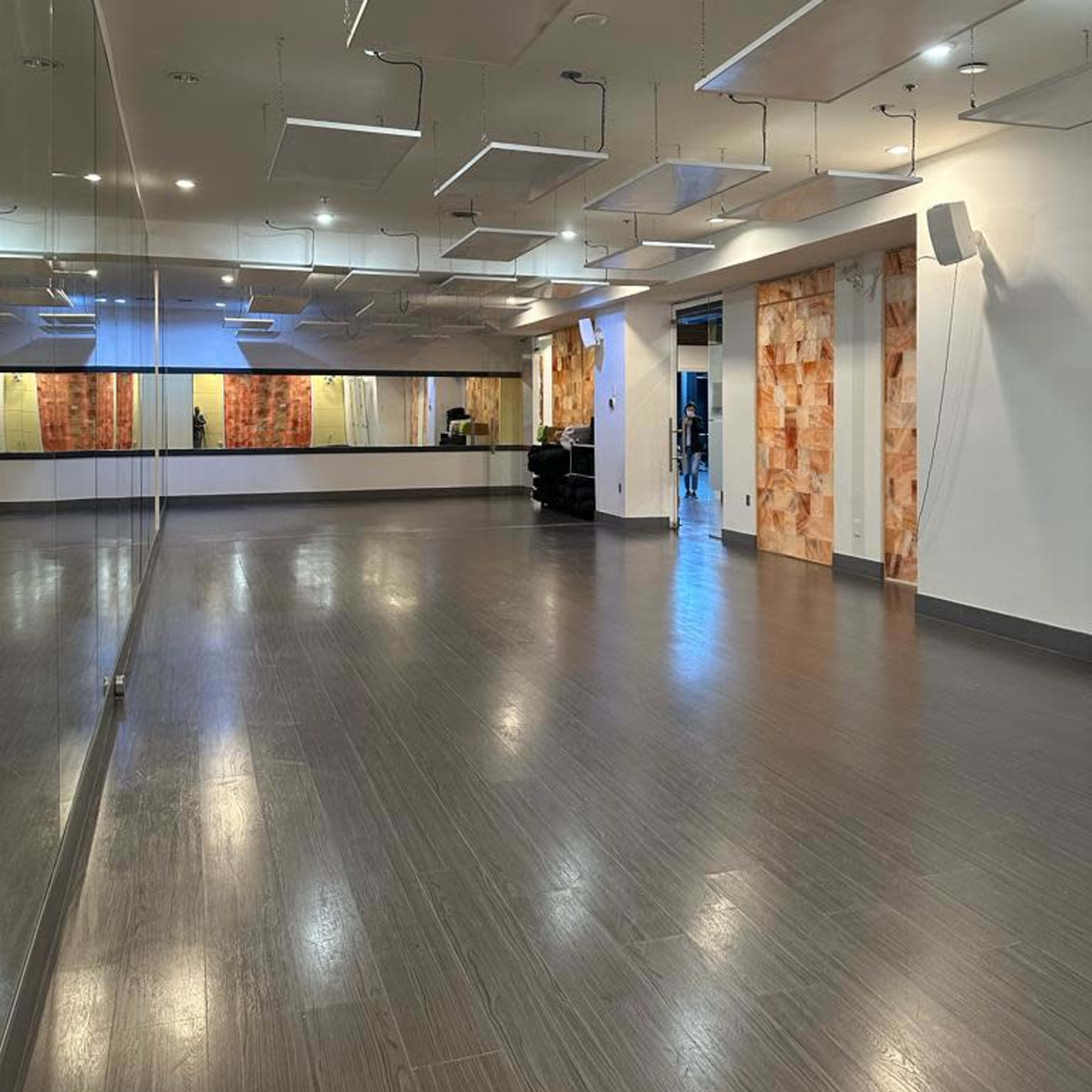 A spacious, well-lit dance studio with mirrored walls and suspended light fixtures.