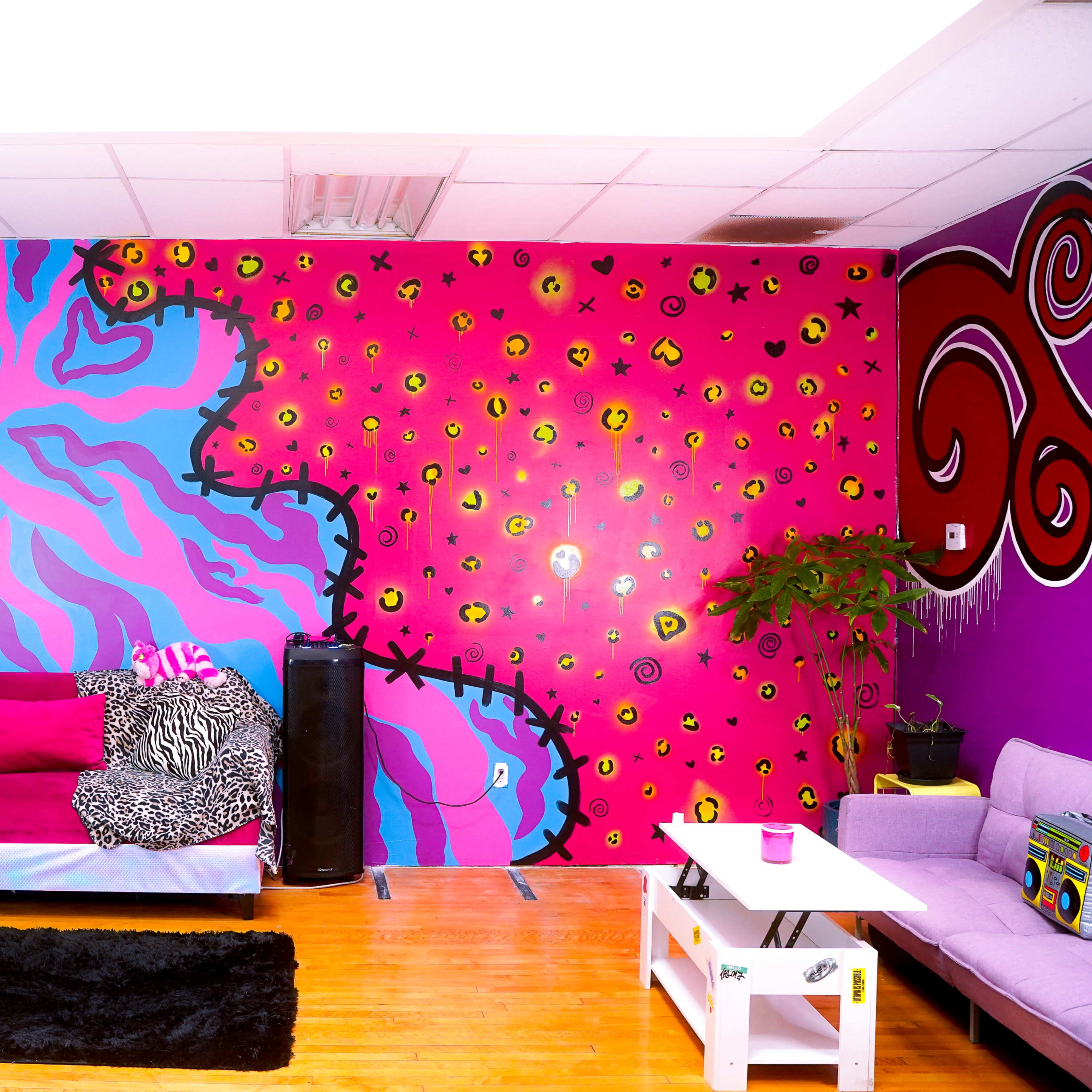 A vibrant lounge area with a pink and purple mural on the wall, a sectional sofa, and a small table on a wooden floor.
