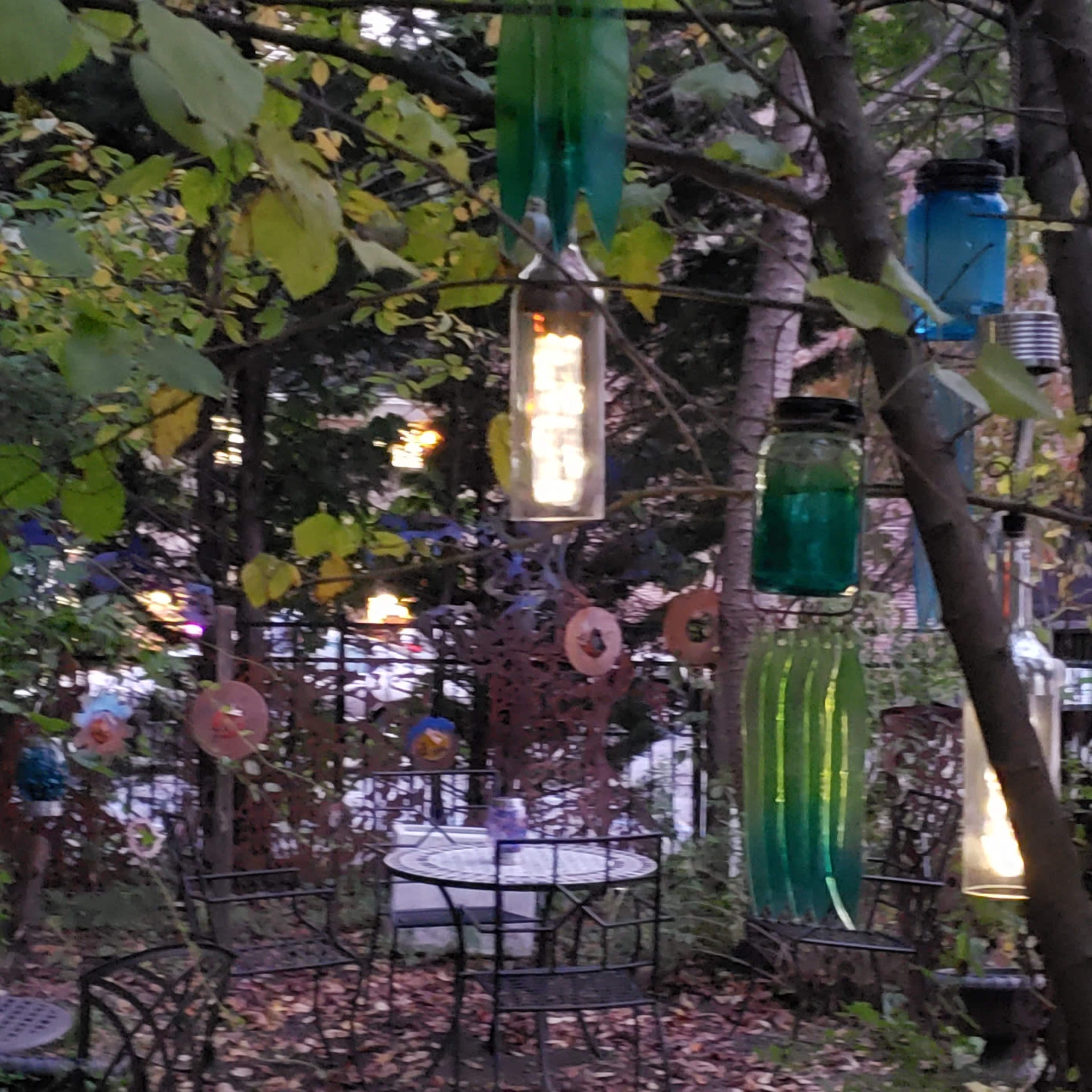 A garden area with metal bistro tables and chairs surrounded by colorful hanging glass jars and autumn leaves.