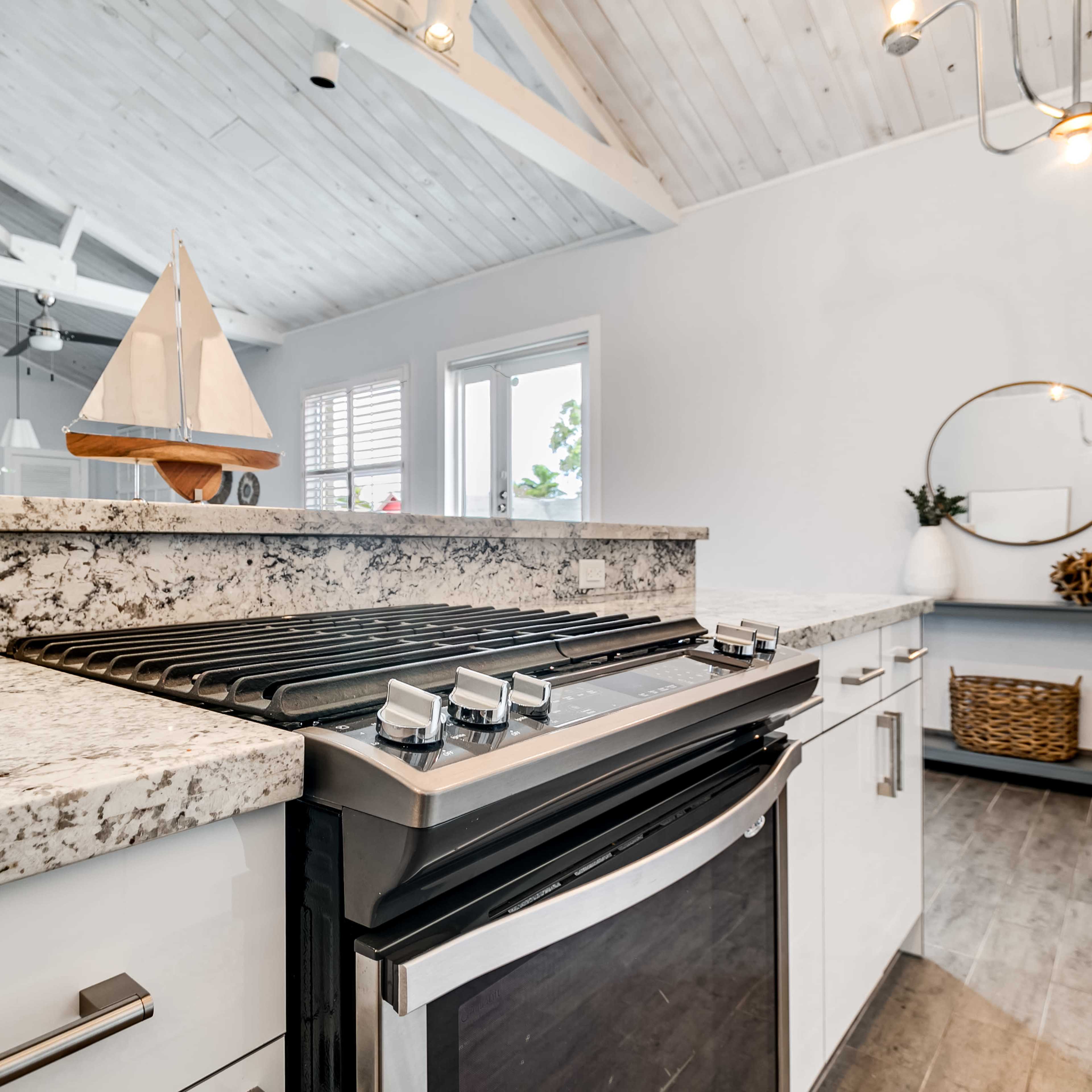 A modern kitchen with a granite countertop, a stainless steel gas stove, and a decorative sailboat on display.