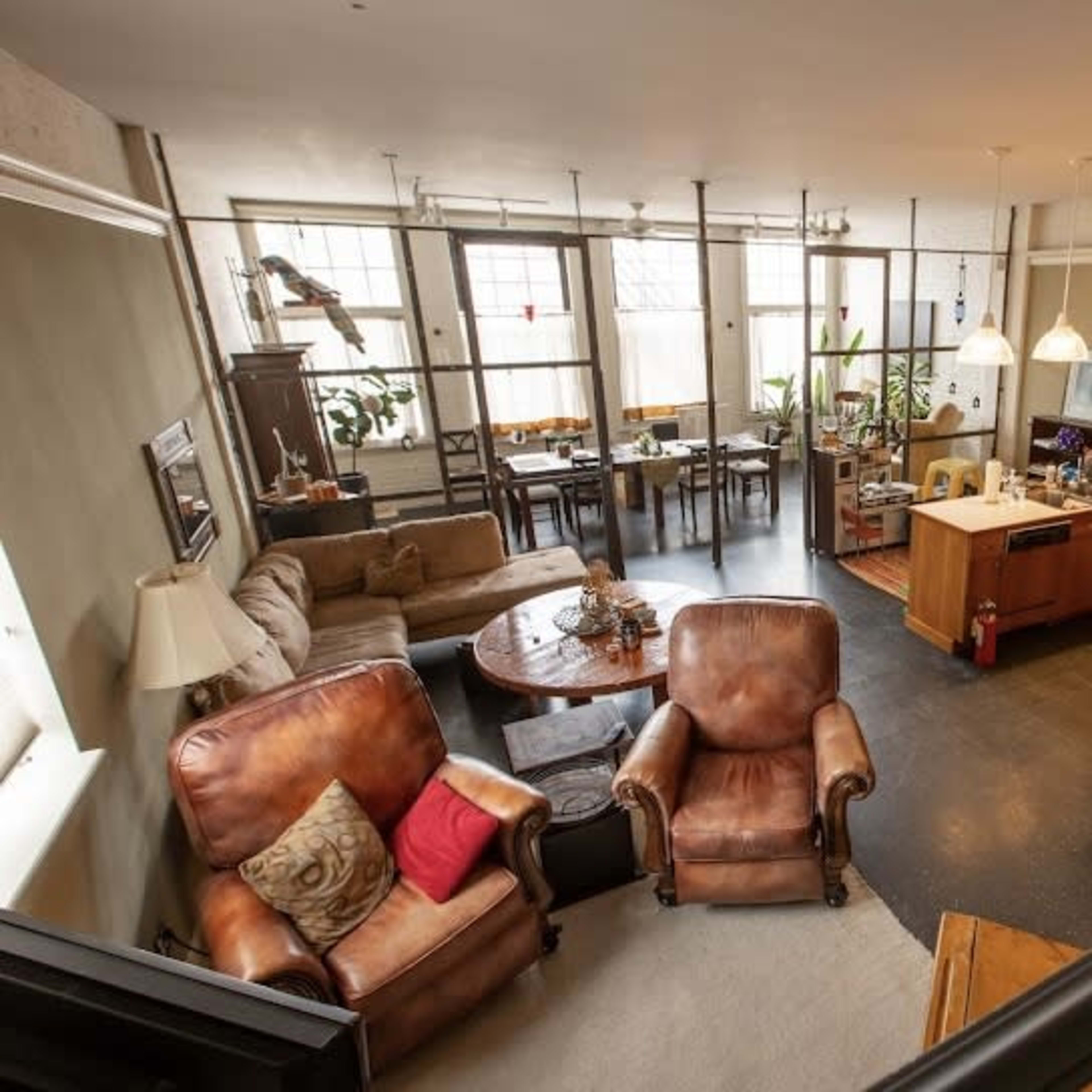 A spacious, open-concept loft with a kitchen, living area, and dining space, featuring large windows and modern furnishings.