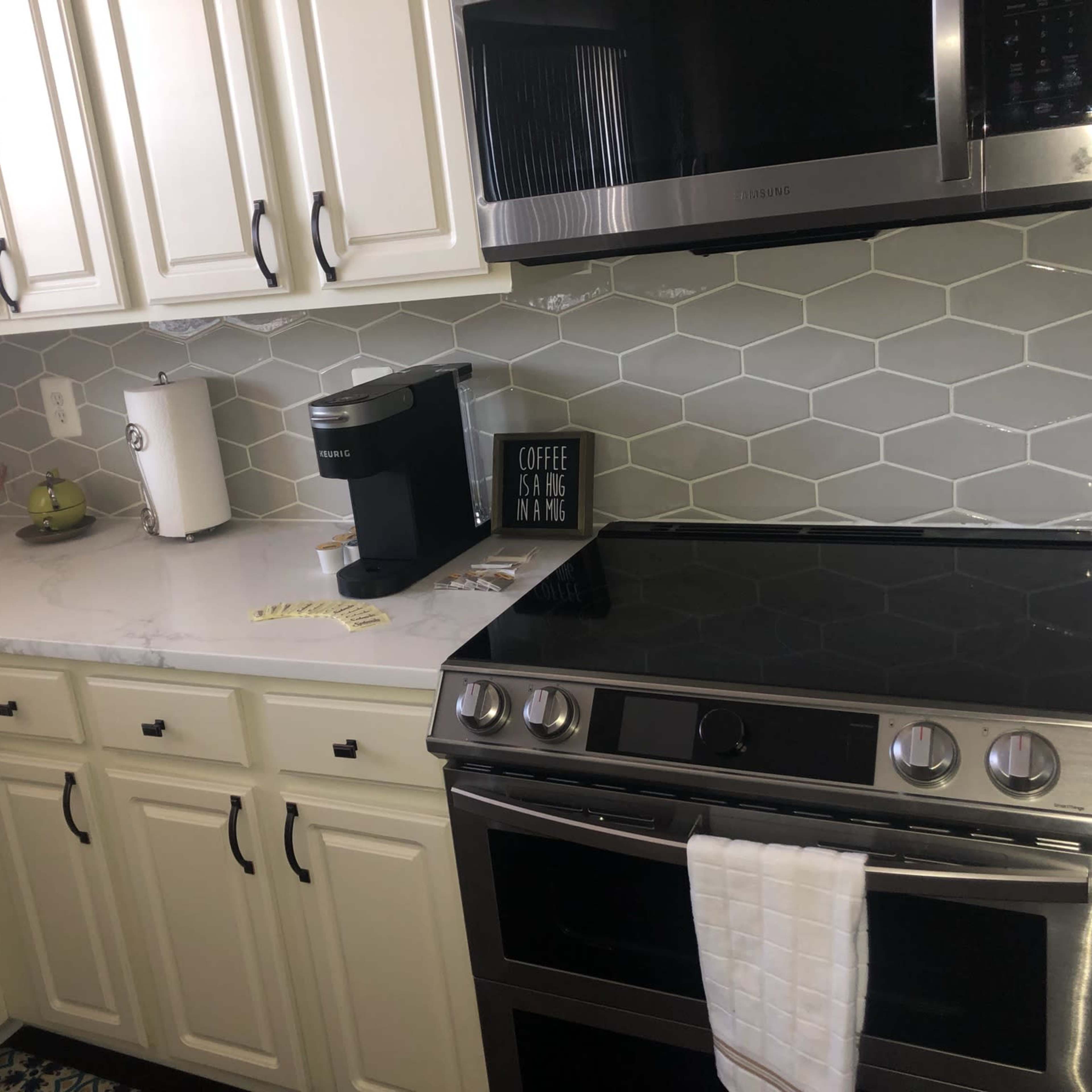 A modern kitchen with white cabinets, a gray hexagonal tile backsplash, a coffee maker, and a stainless steel stove.
