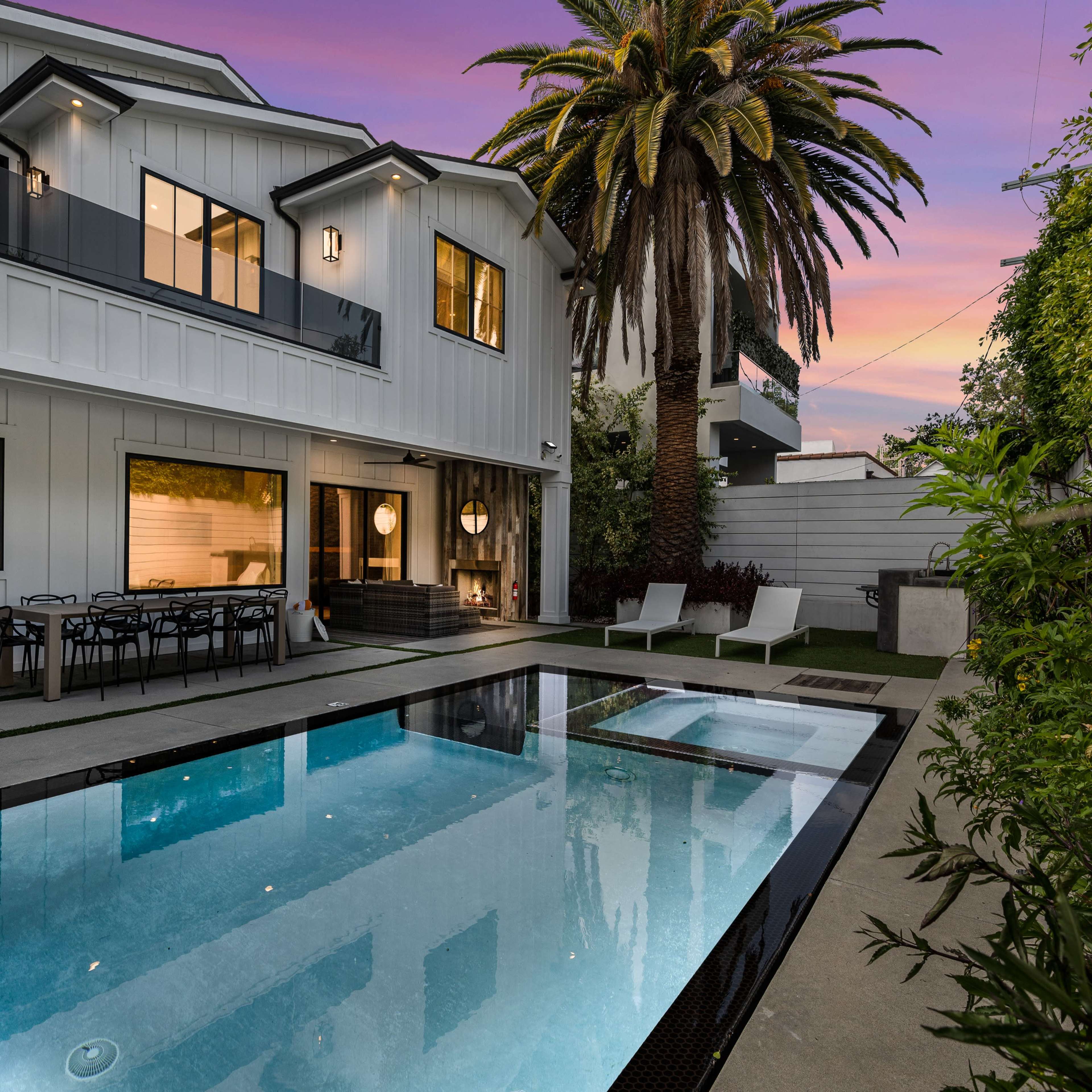 A modern house with a pool and palm trees is set against a colorful sunset sky.
