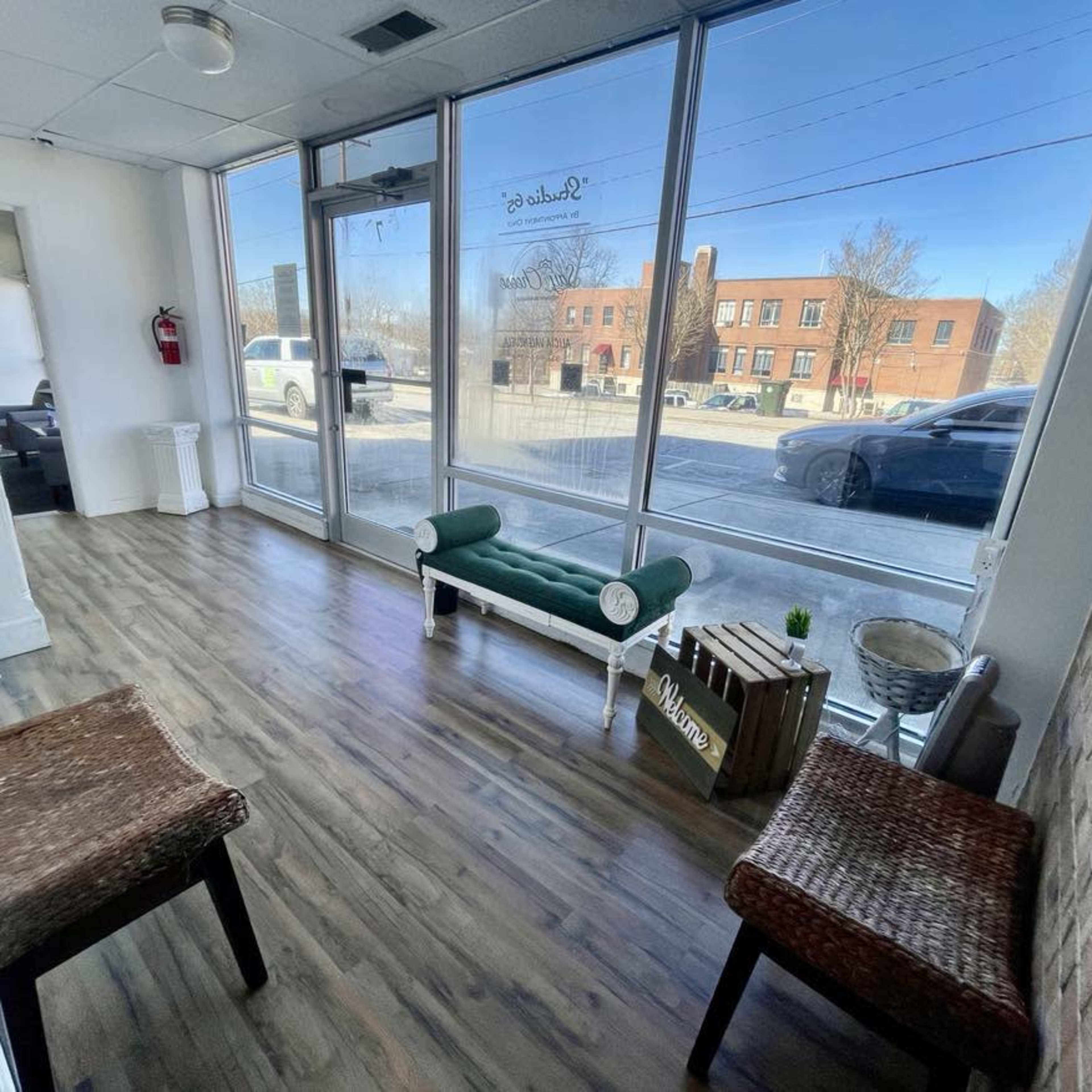A waiting area with two woven chairs, a green bench, and large windows allowing natural light to enter.