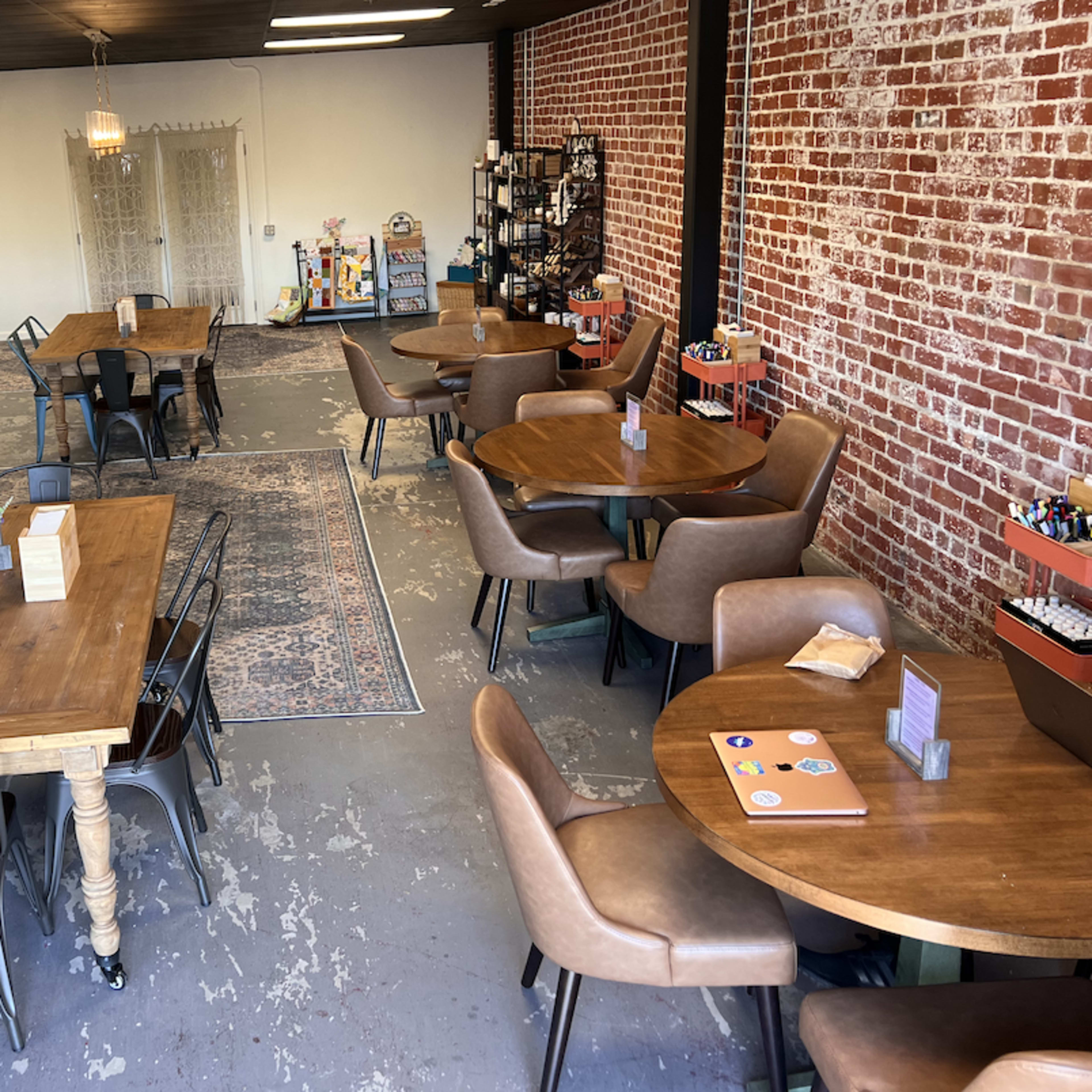 A spacious café interior features wooden tables, chairs, and a brick wall, with a service counter and decorative items in the background.