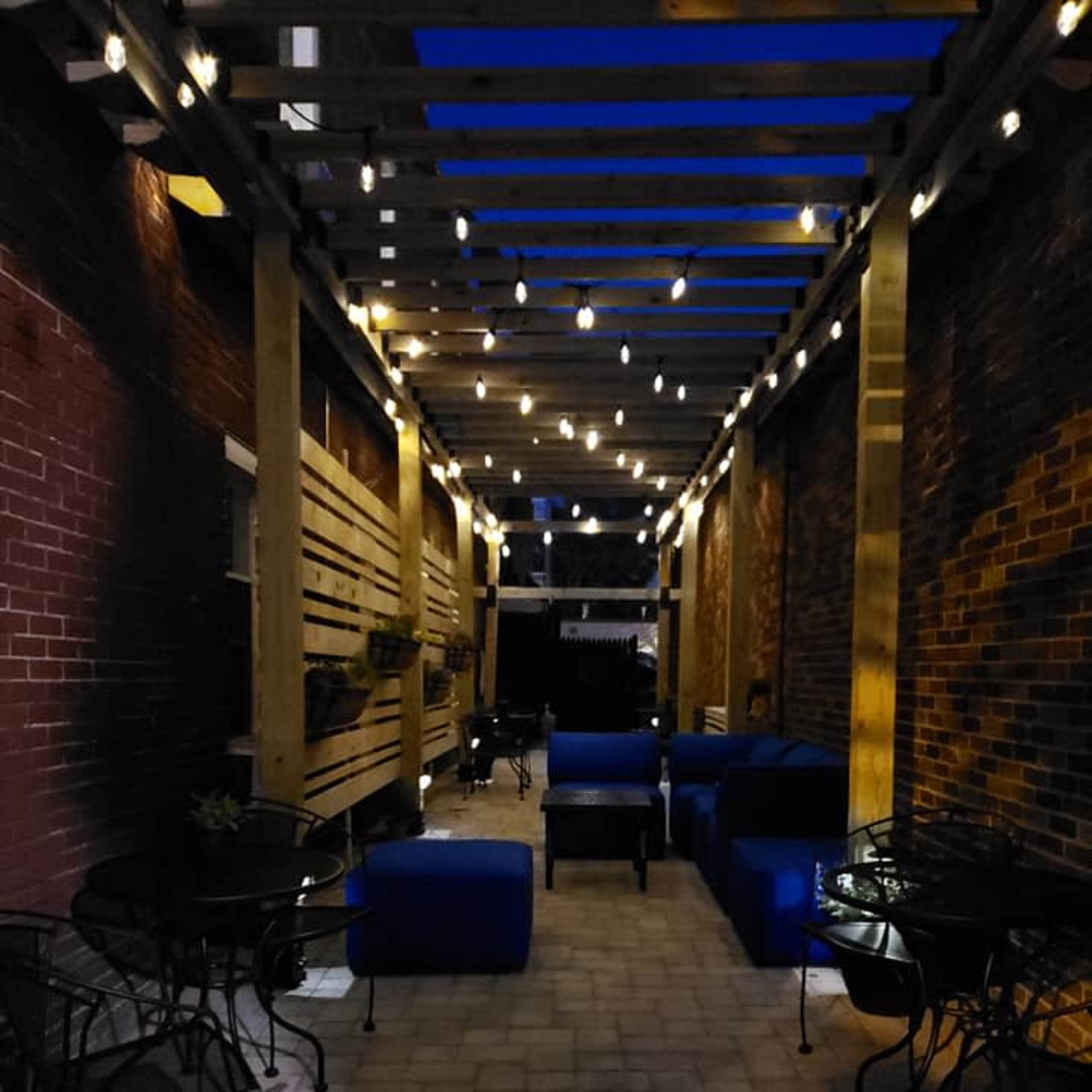 A well-lit outdoor seating area featuring blue furniture, string lights, and brick walls on either side.