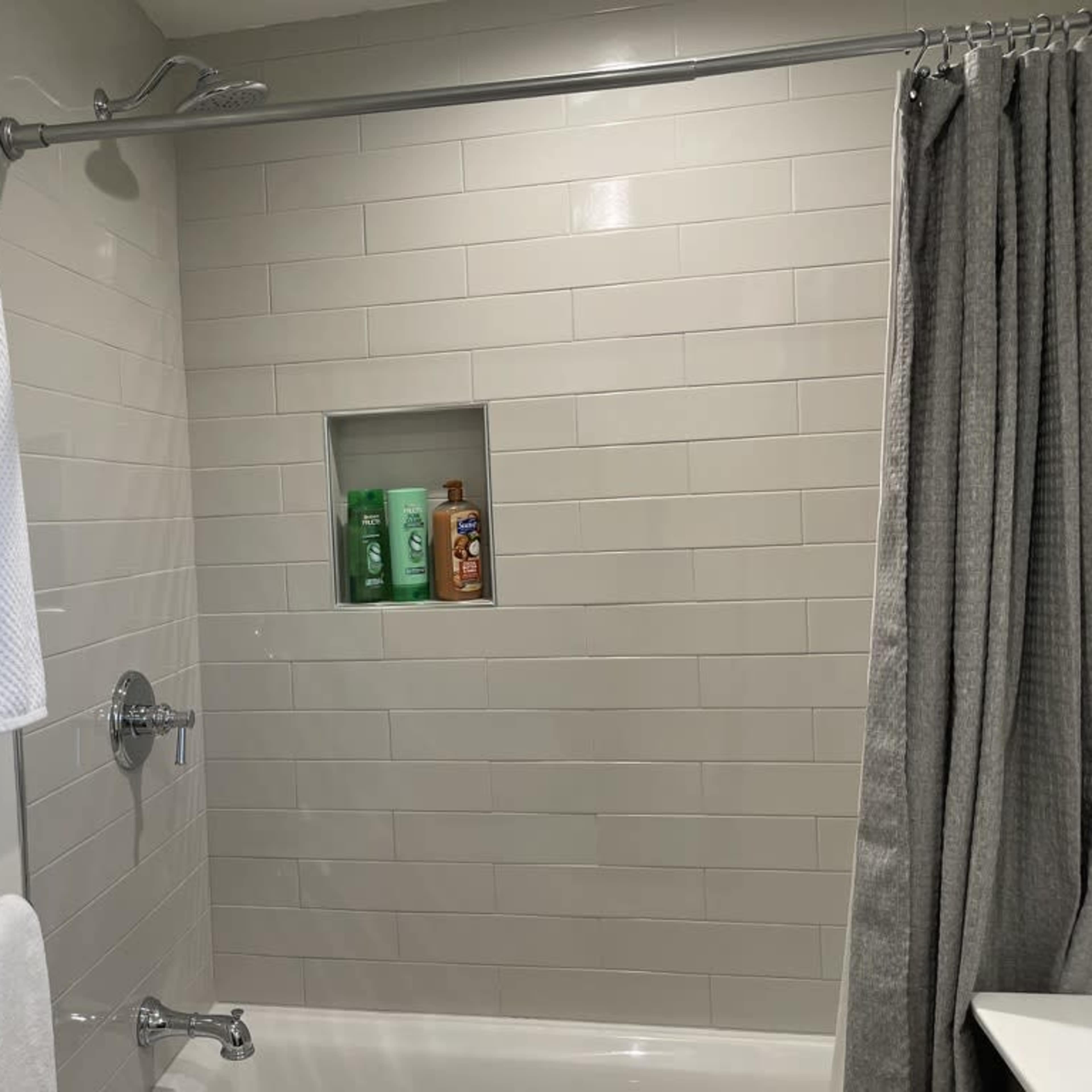 A clean shower area with a tiled wall, a small niche for toiletries, and hanging towels.