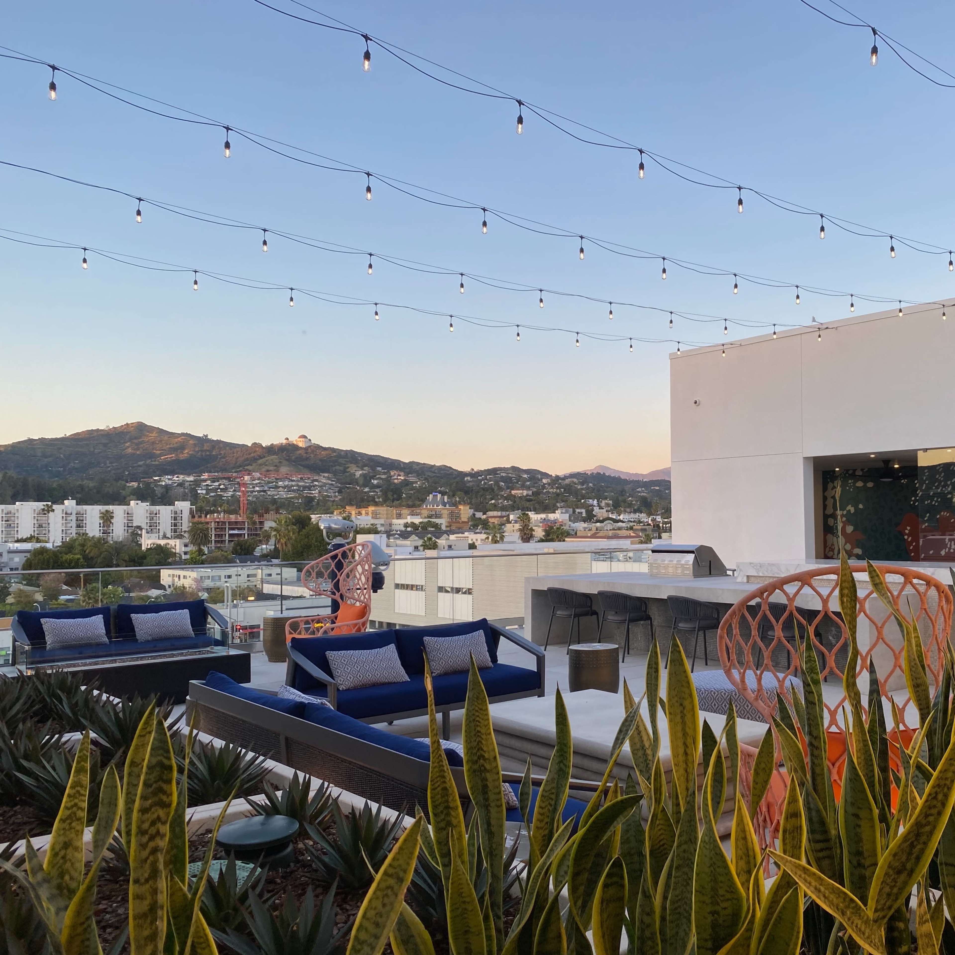 A rooftop terrace features seating arrangements and string lights overlooking a scenic view of a mountainous landscape.