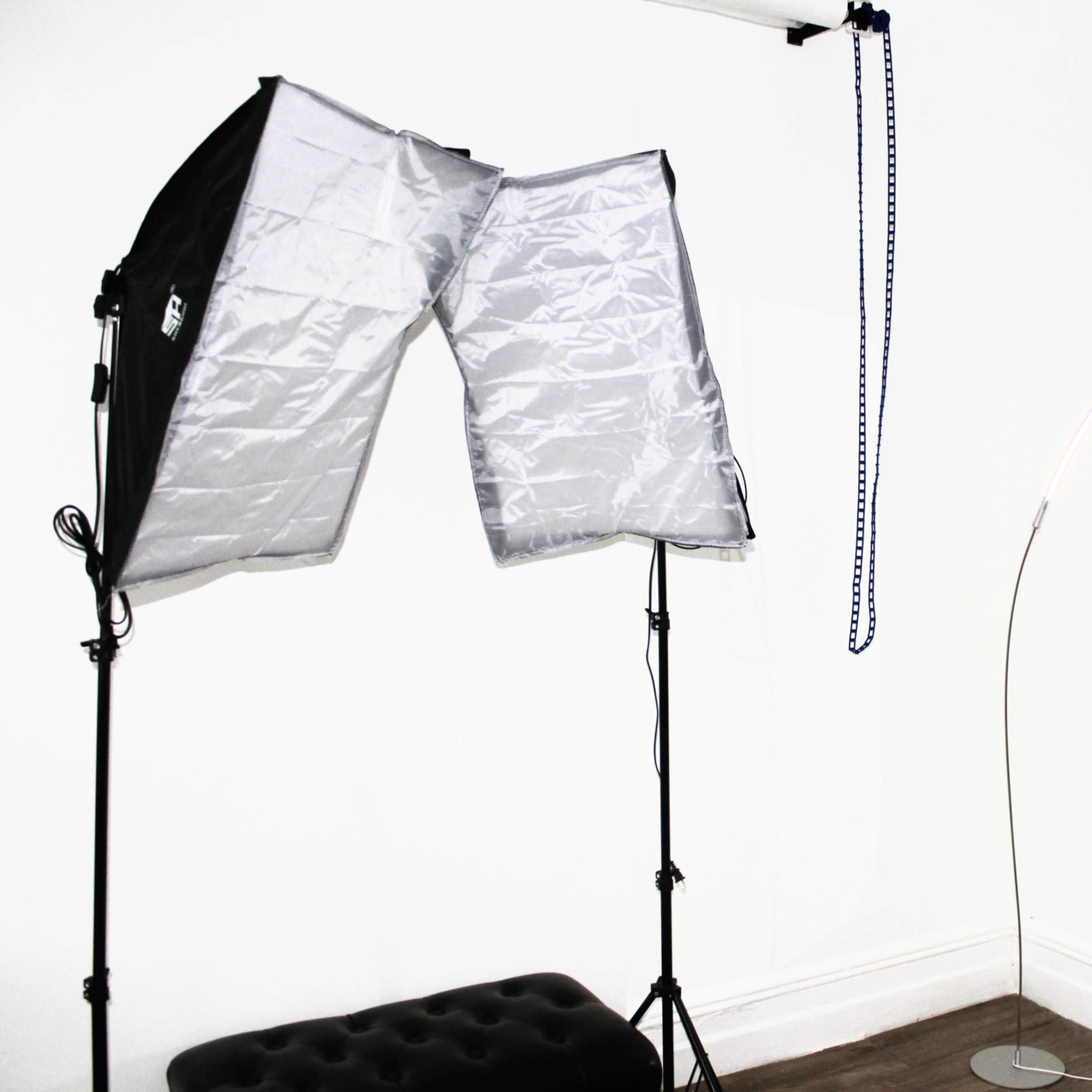 A corner of a studio featuring a lighting setup with softboxes, a floor lamp, and a wall-mounted mirror.