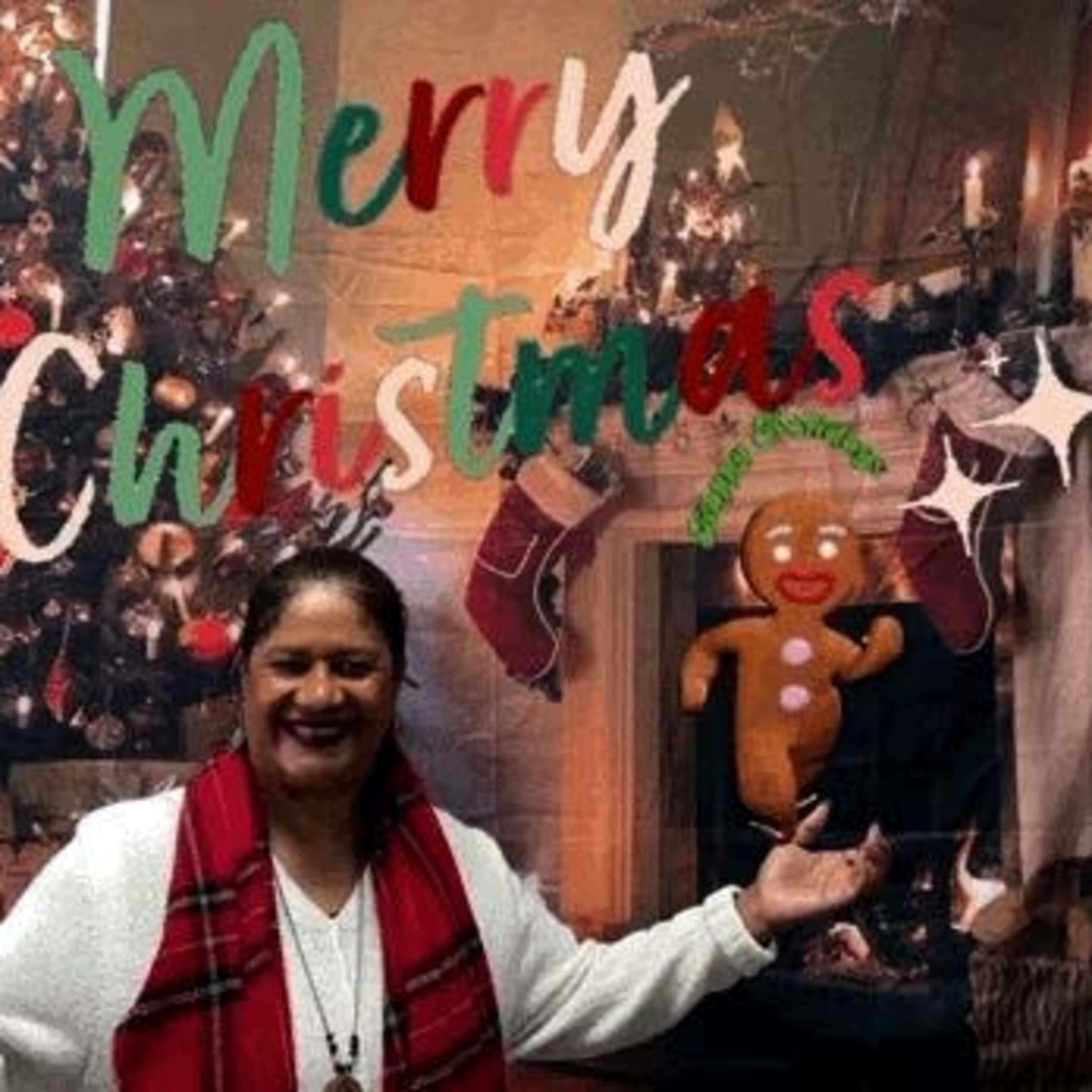 A person stands with arms outstretched in front of a decorated Christmas tree and a festive backdrop that reads "Merry Christmas."