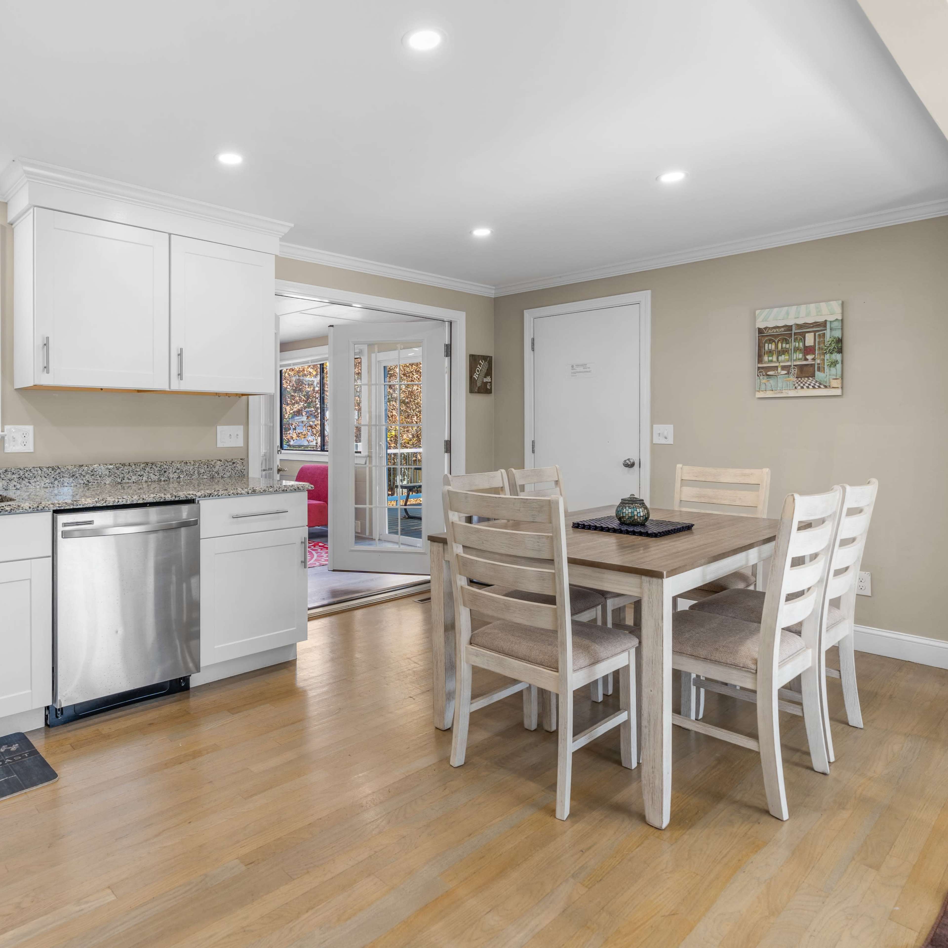 A modern kitchen with white cabinets, granite countertops, a stainless steel dishwasher, and a dining table with six chairs.