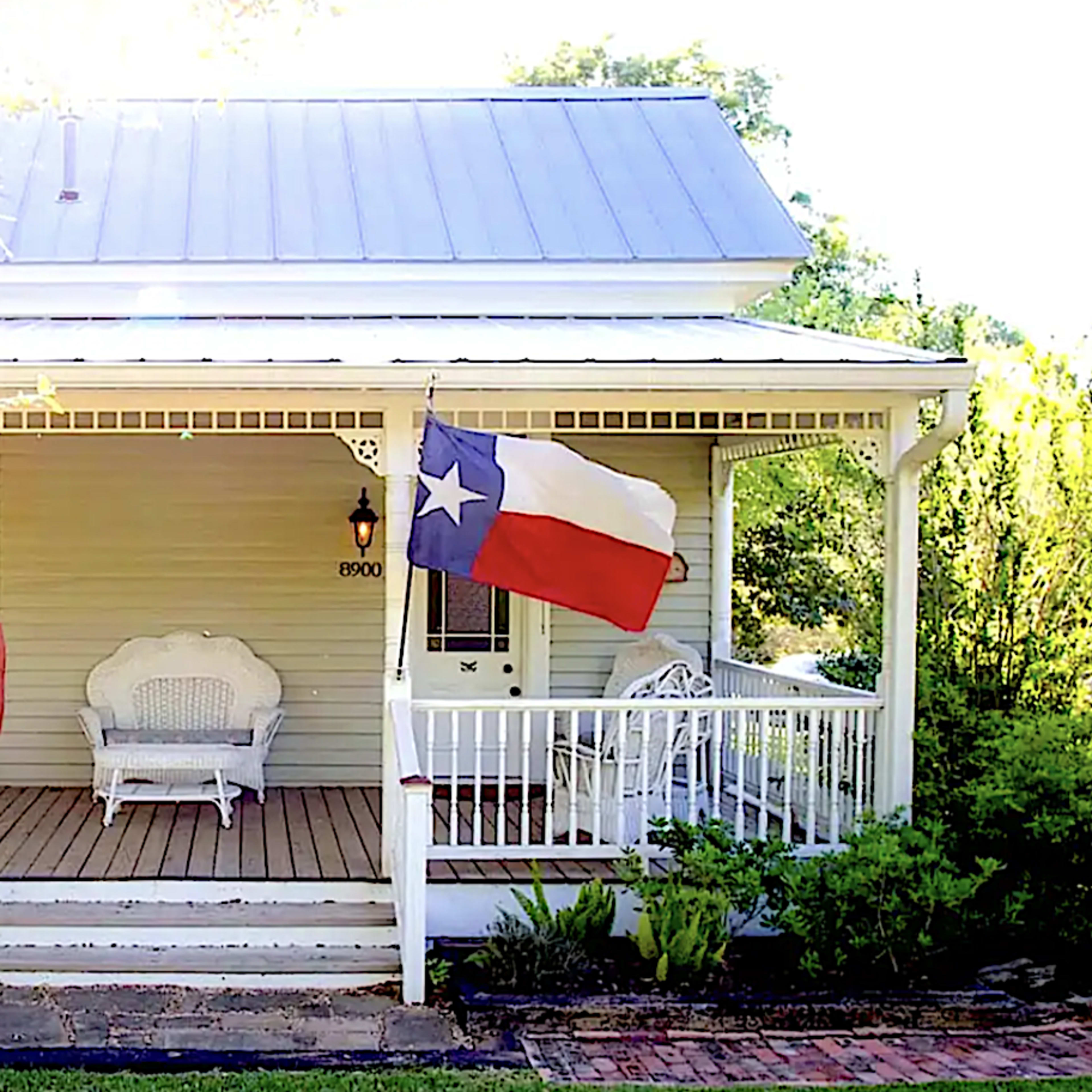 A house with a porch displays an American flag and a Texas state flag.