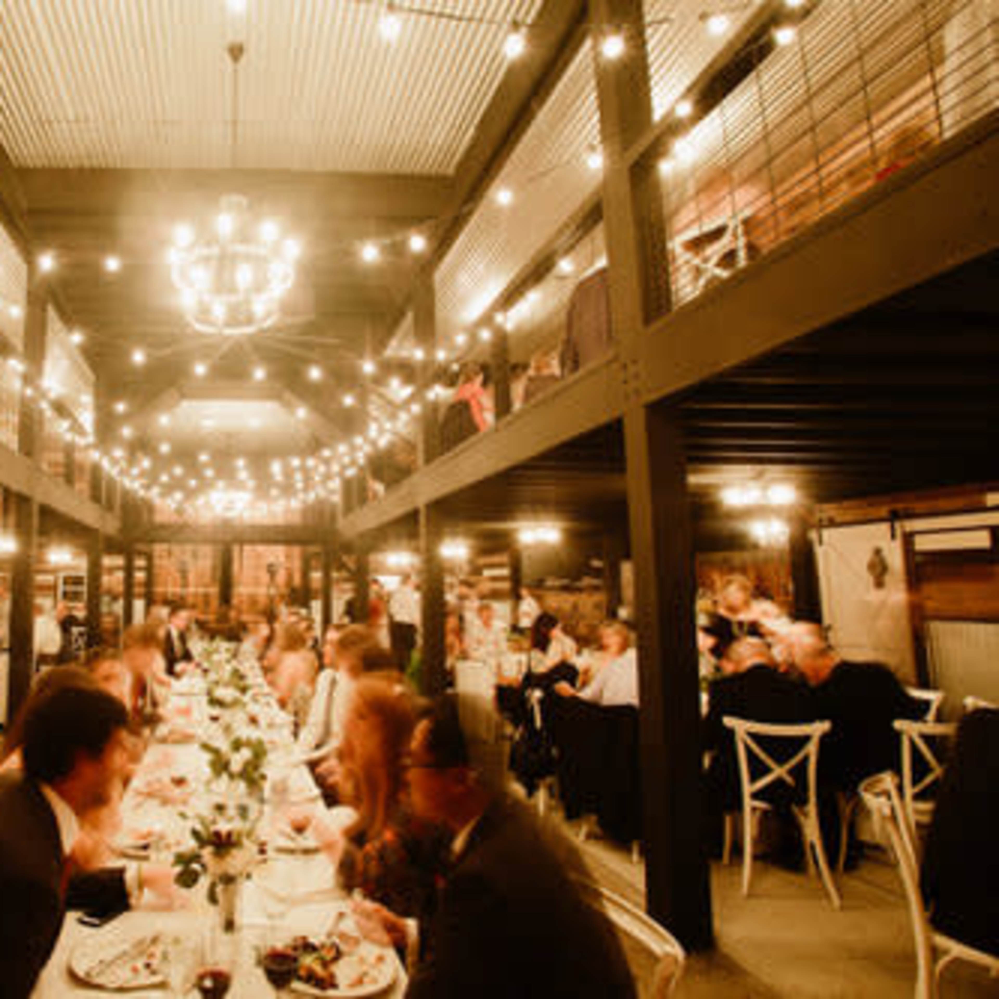 A large dining area features a long table set for a formal dinner, with guests seated and enjoying a meal under decorative lights.