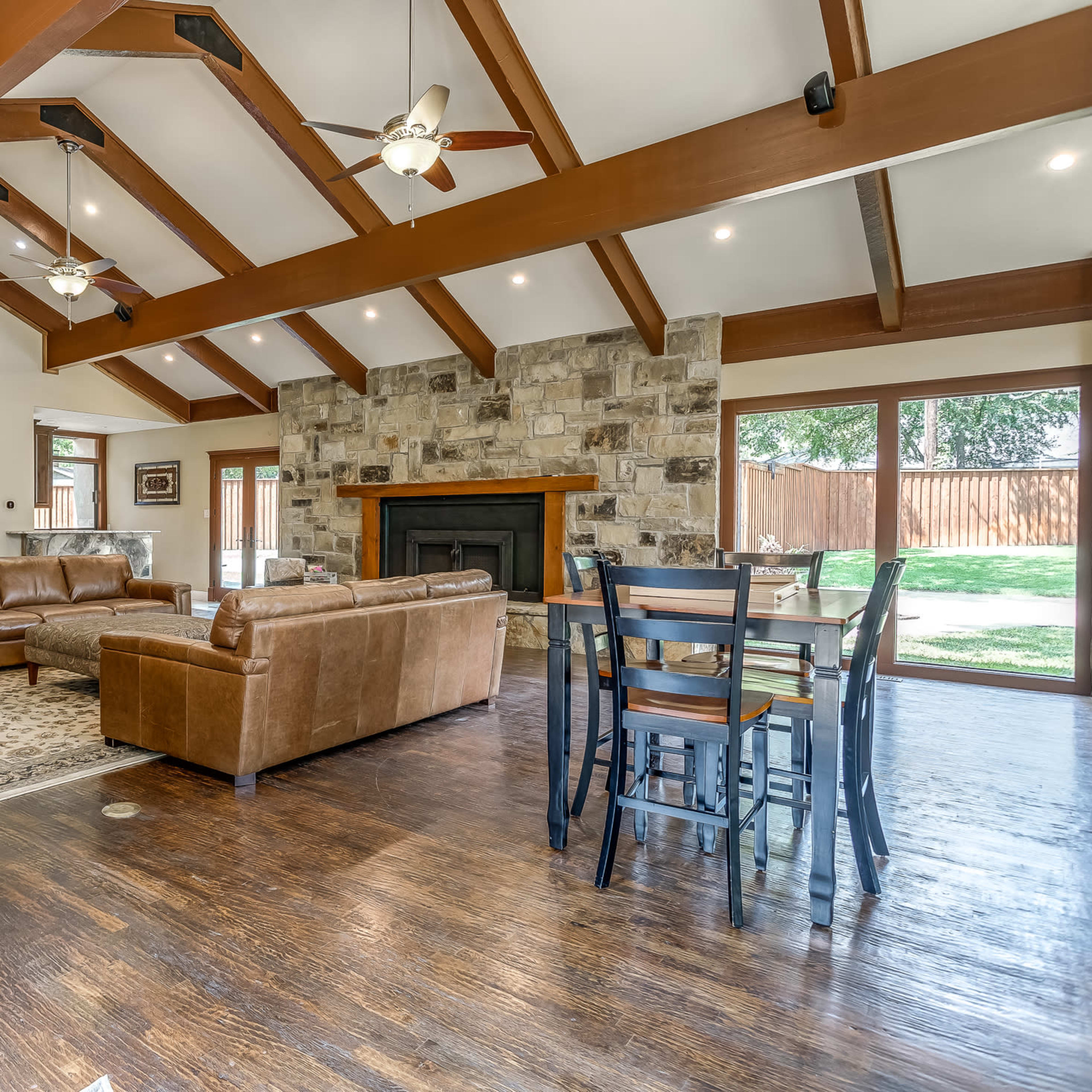 A spacious living room with wooden beams, a stone fireplace, and a dining area featuring a wooden table and chairs.