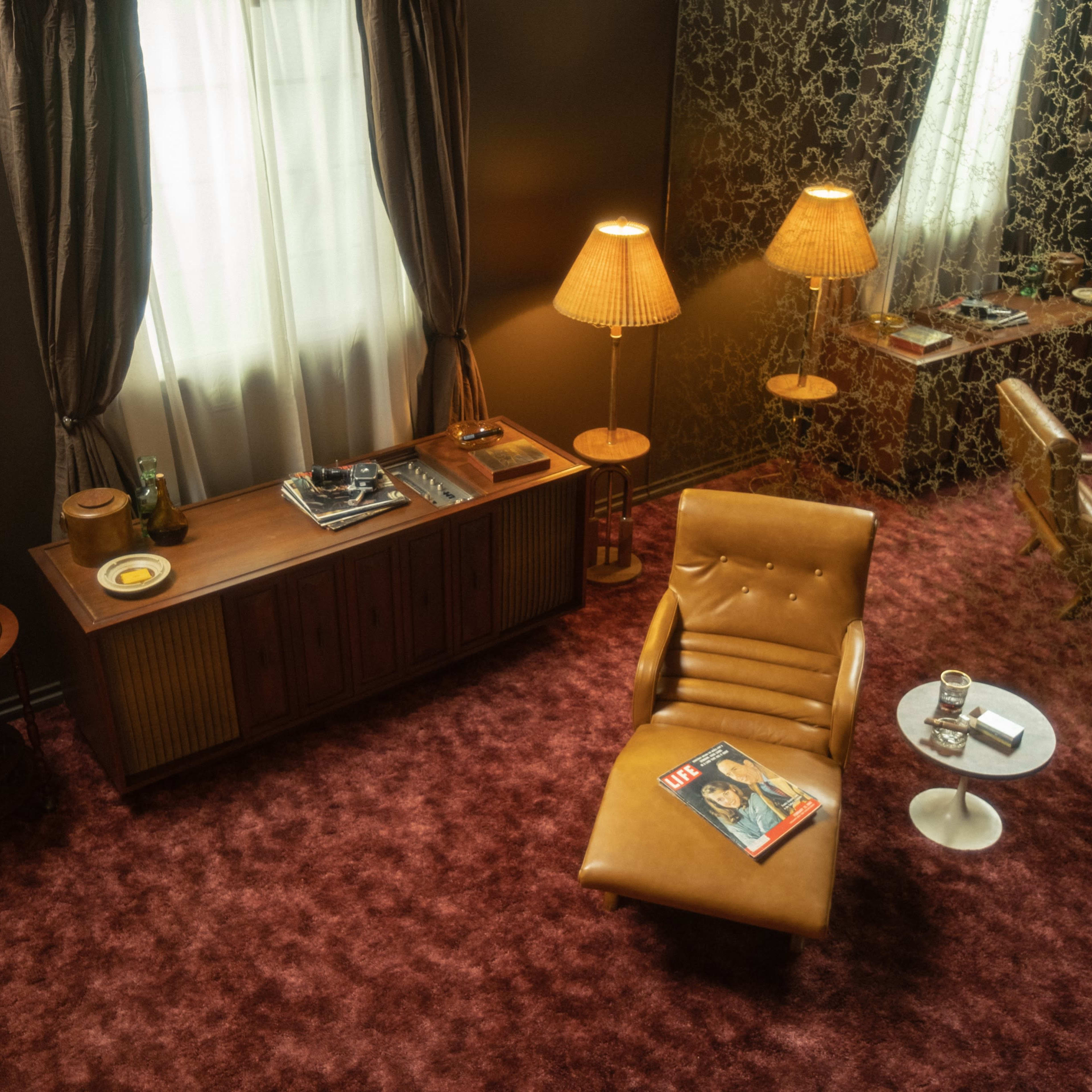 A cozy living room with a brown leather chair, a wooden sideboard, and a reflective wall, illuminated by two lamps.