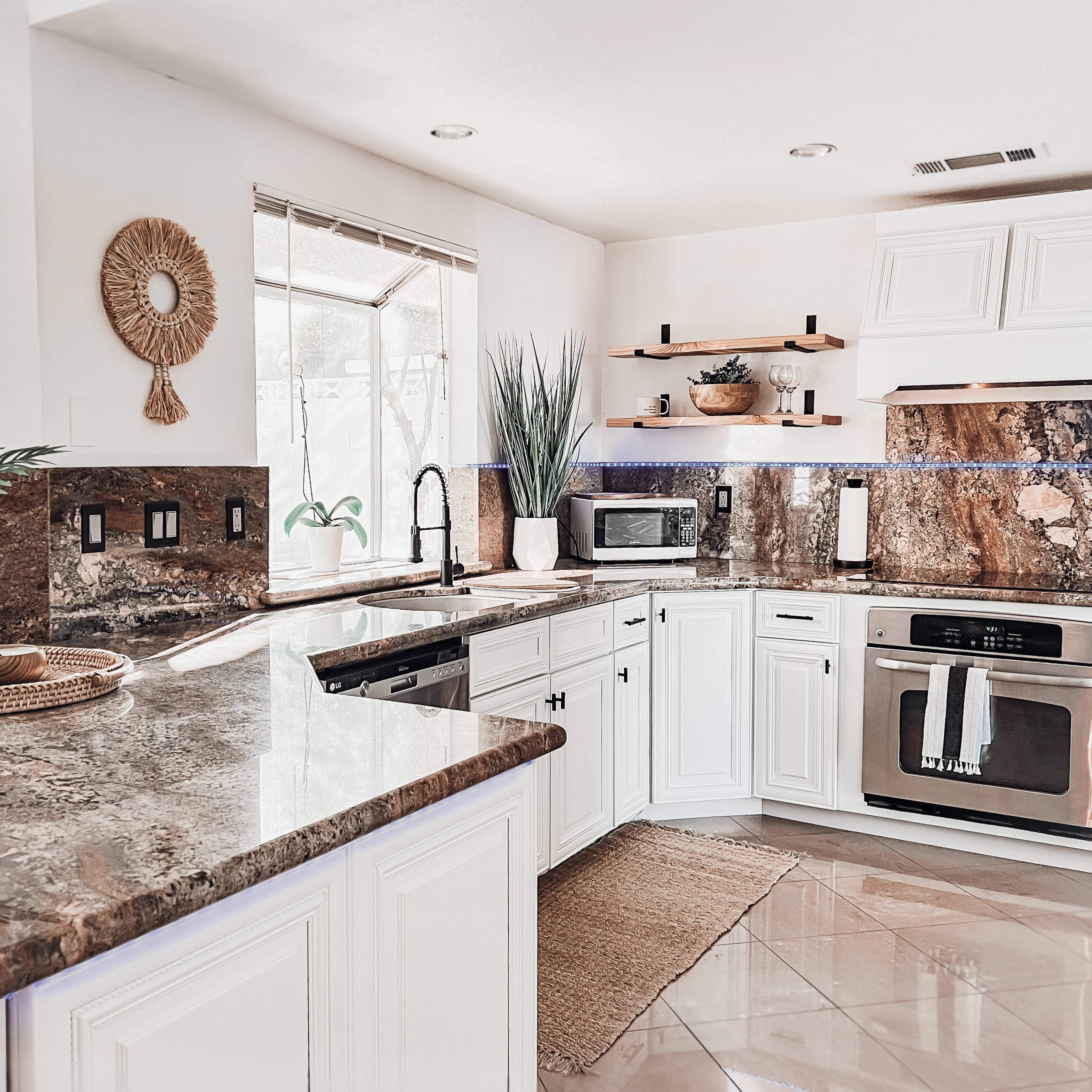 A modern kitchen with white cabinets, a large granite countertop, and natural light pouring in through the windows.