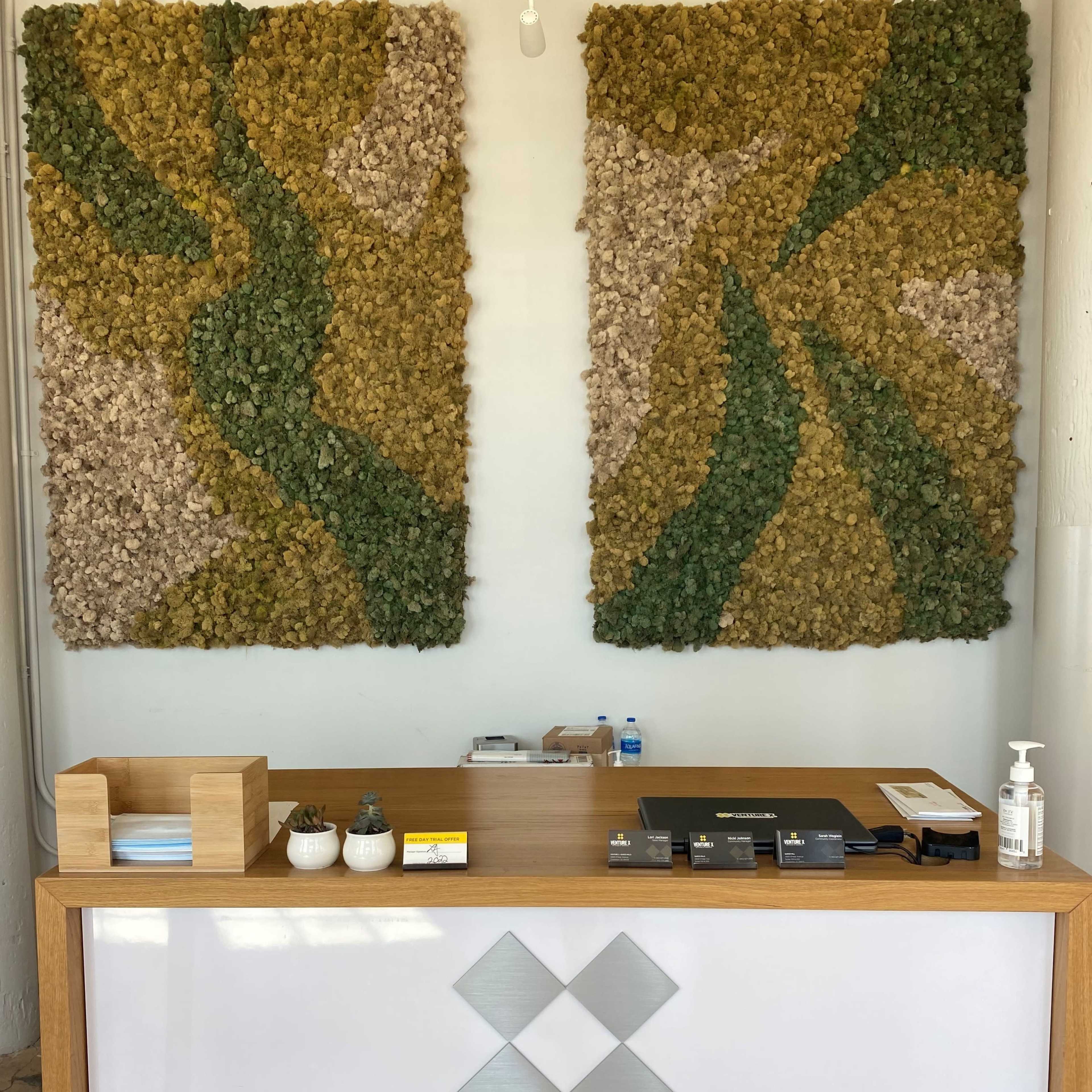 A wooden reception desk displays the logo "Venture X," flanked by two large, textured wall art panels made of greenery.