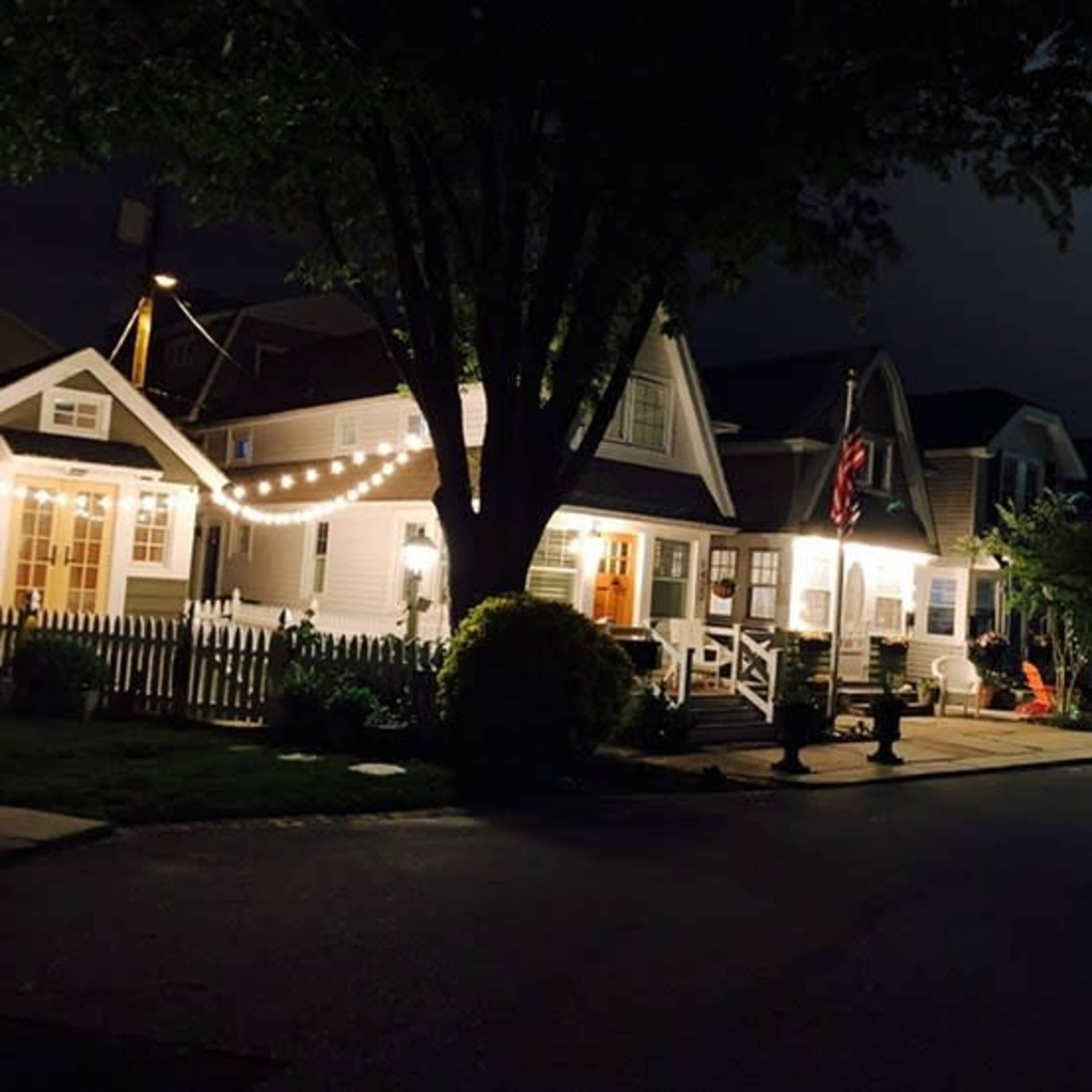 A row of illuminated houses at night, adorned with string lights and featuring a visible American flag.