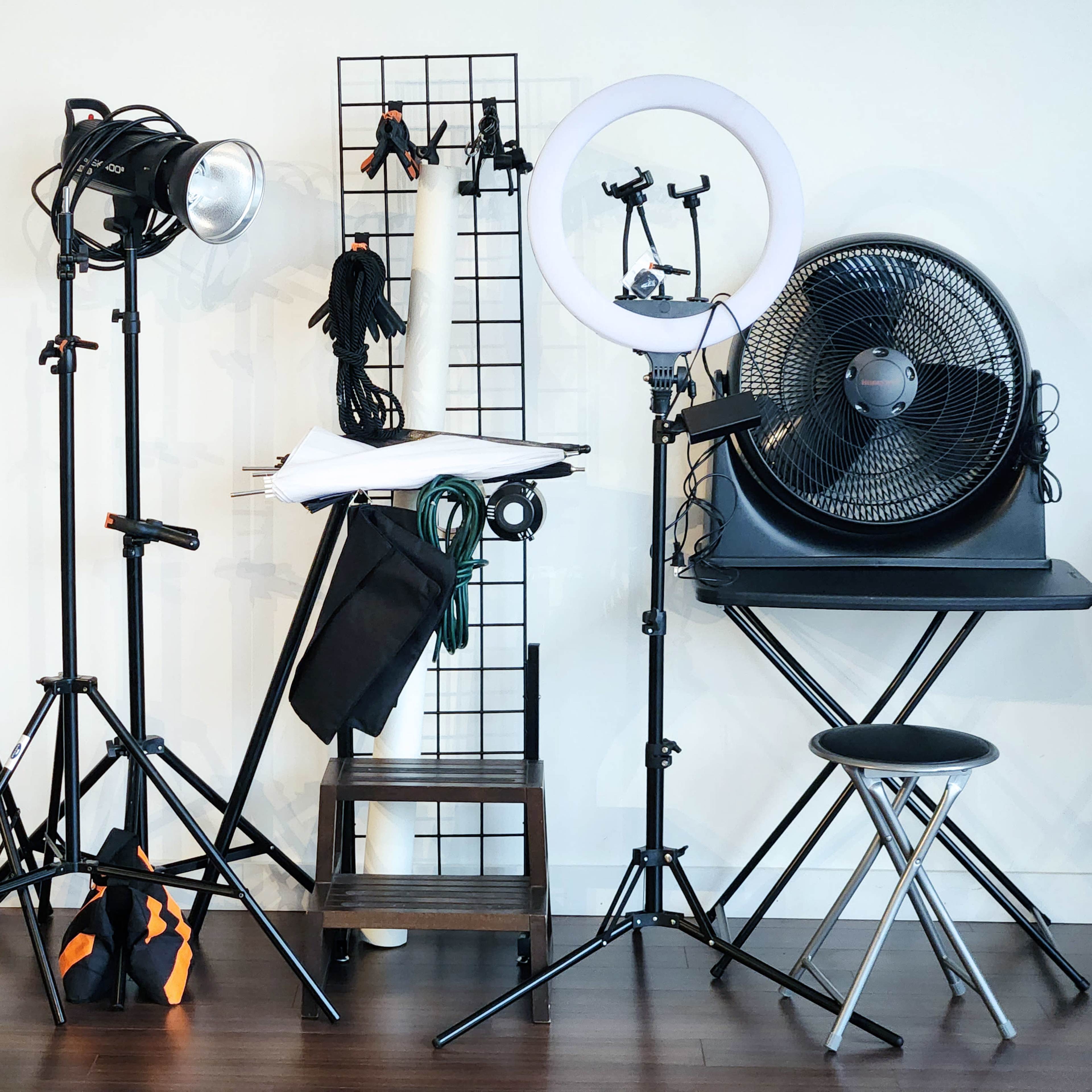 A photography setup featuring various lights, a fan, and a folding table against a wall.