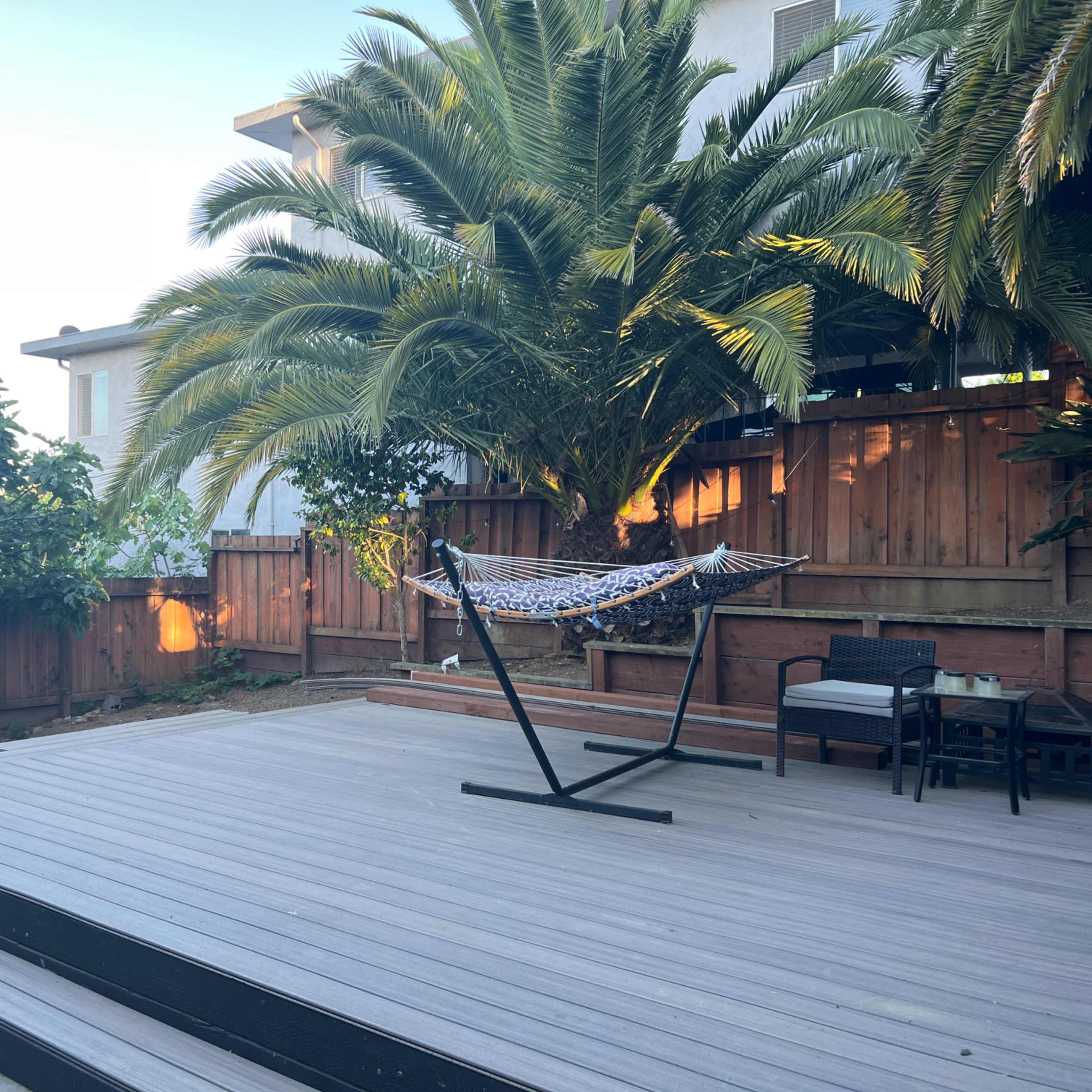 A wooden deck features a hammock hanging between palm trees, with a seating area in the background.