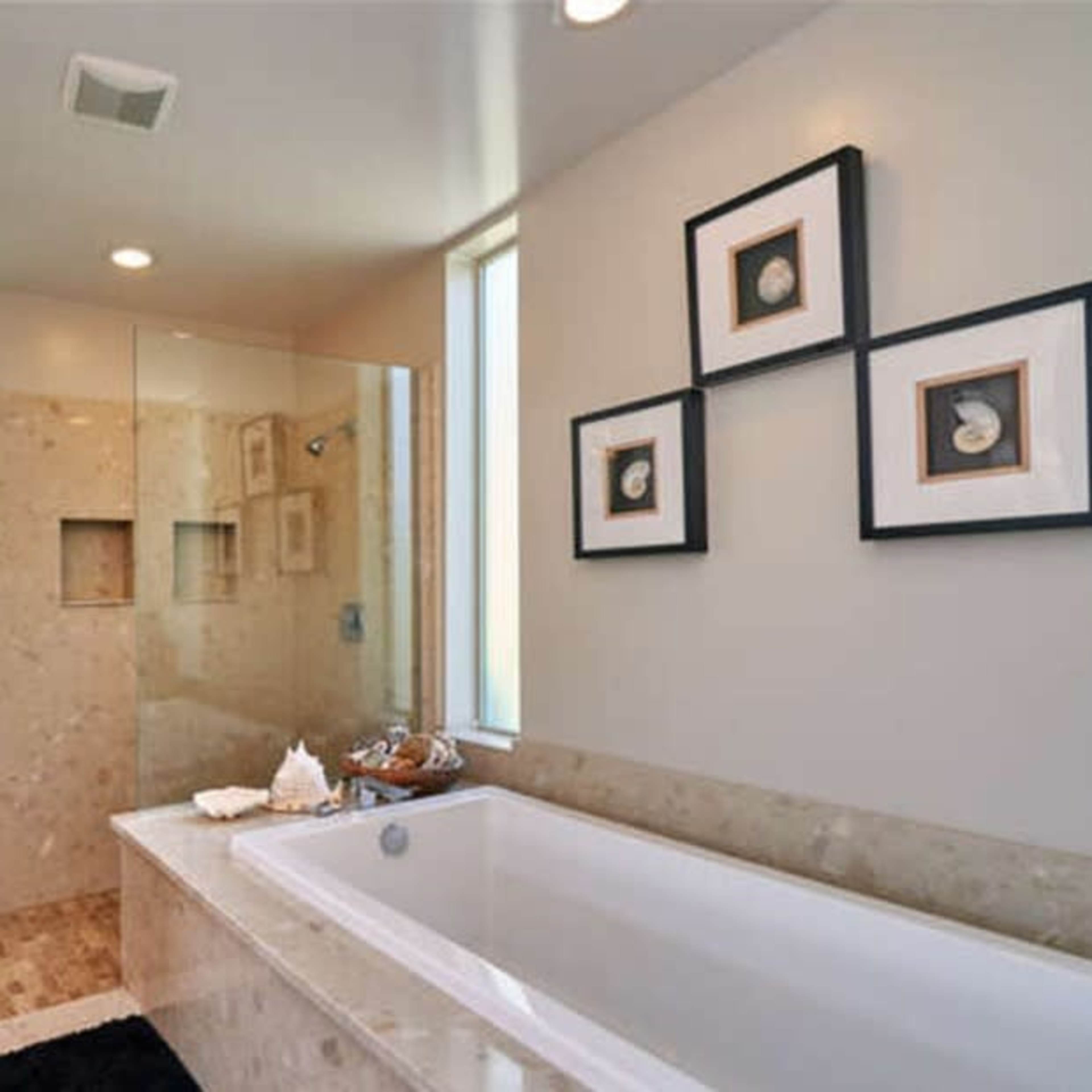 A modern bathroom featuring a large bathtub, a glass shower enclosure, and framed artwork on the wall.