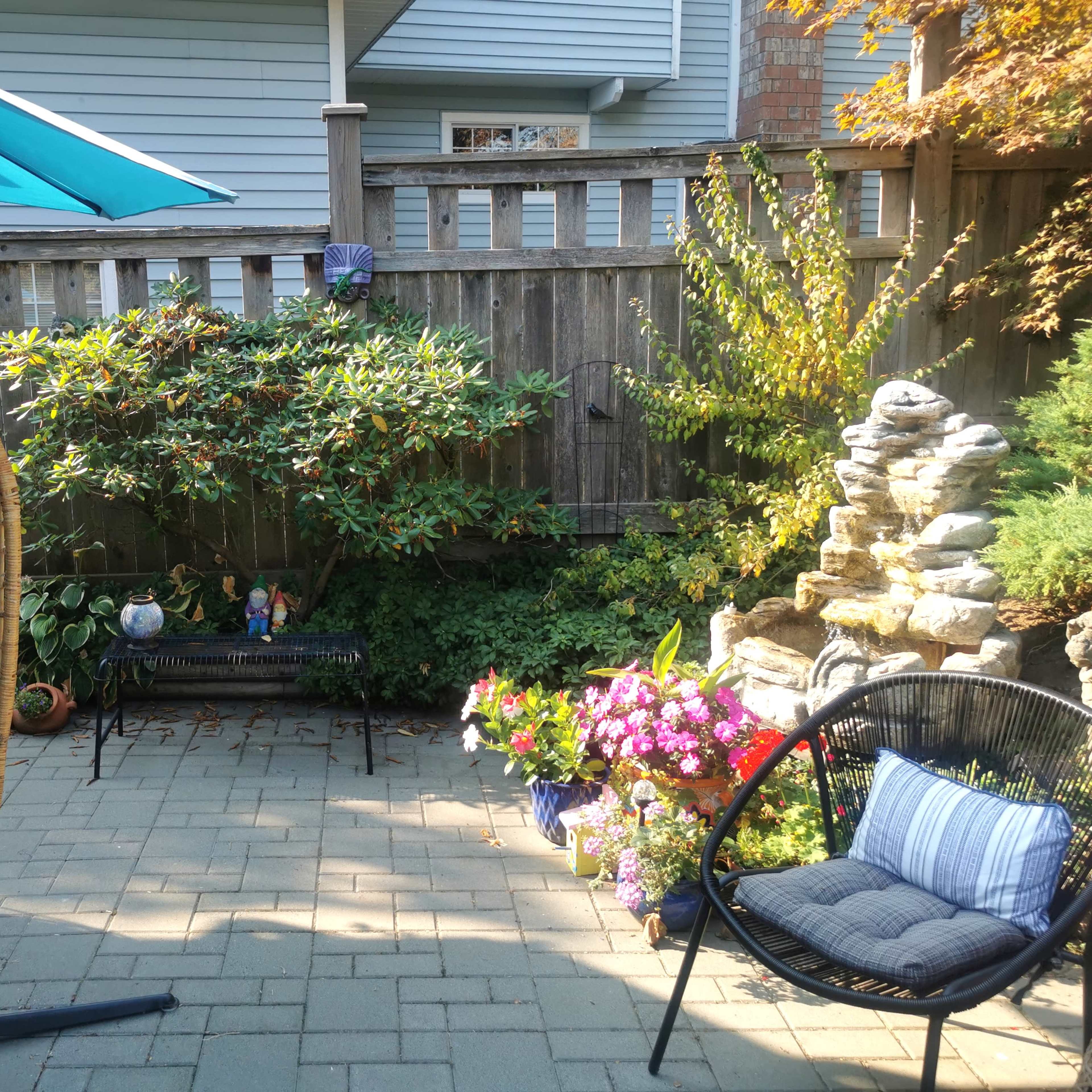 A landscaped backyard with a hanging chair, colorful flowers, and a small stone fountain surrounded by greenery.