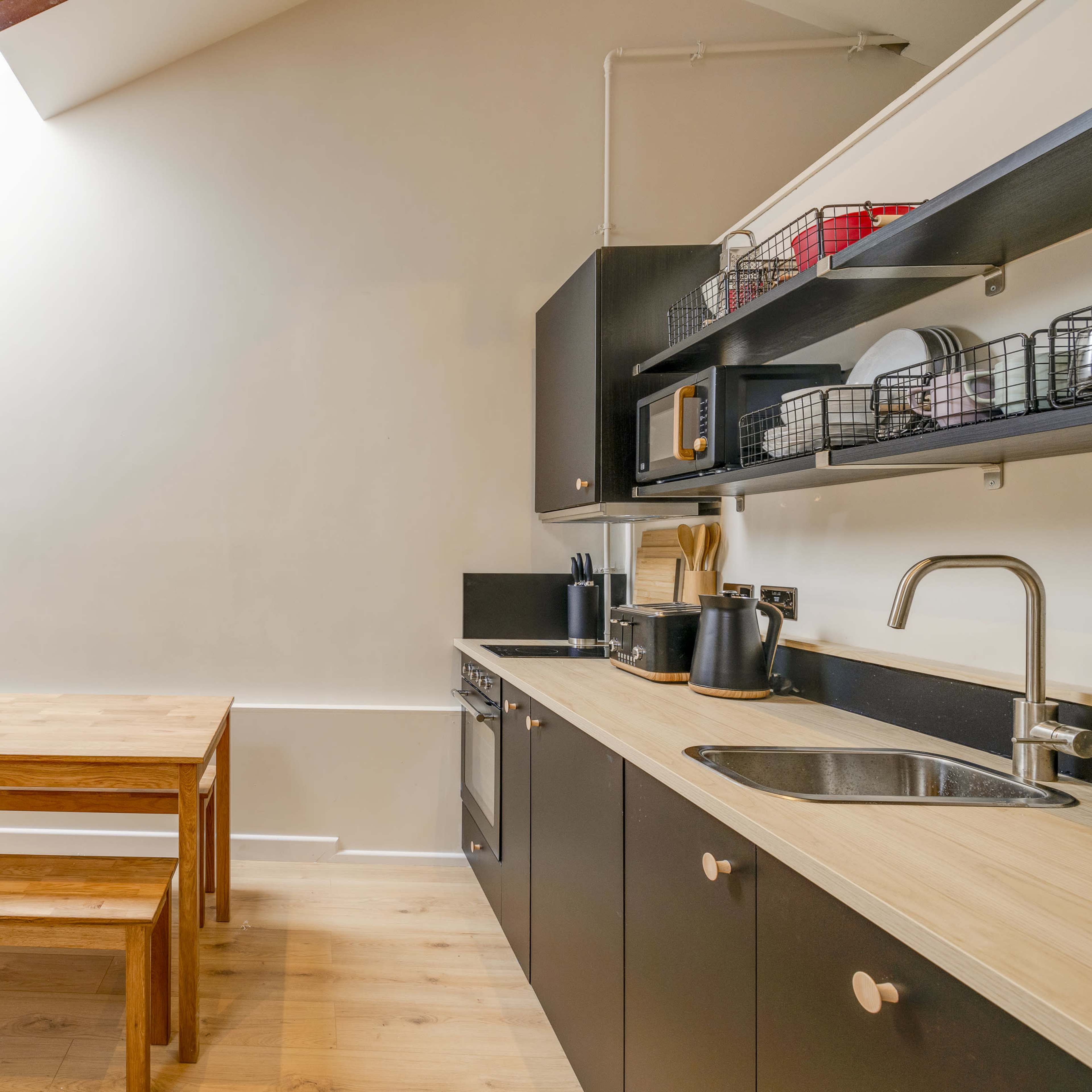 A modern kitchen featuring a wooden table with benches, dark cabinetry, and an open layout illuminated by a skylight.