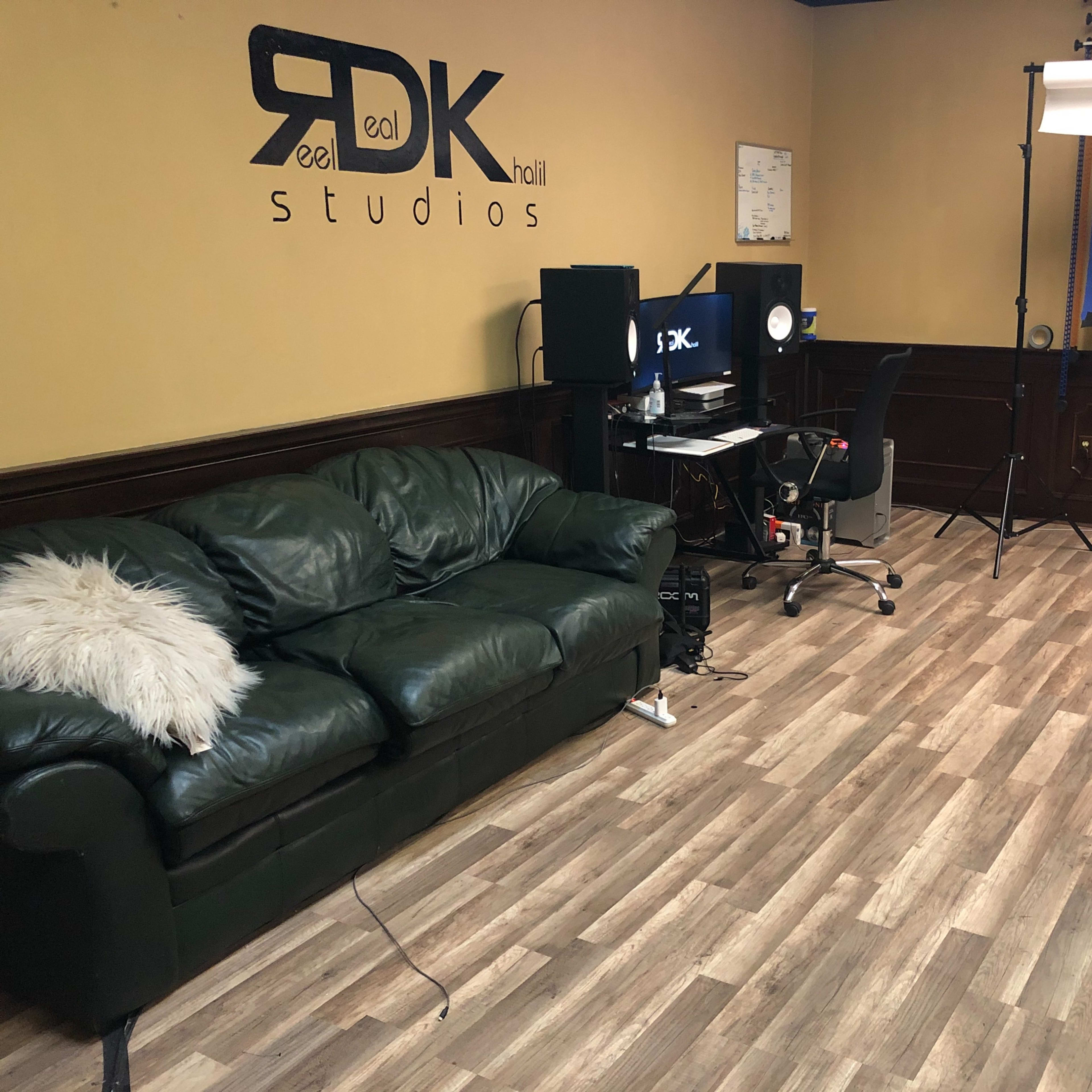A green leather sofa, a desk with a computer setup, and a lighting backdrop in a studio with wooden flooring.